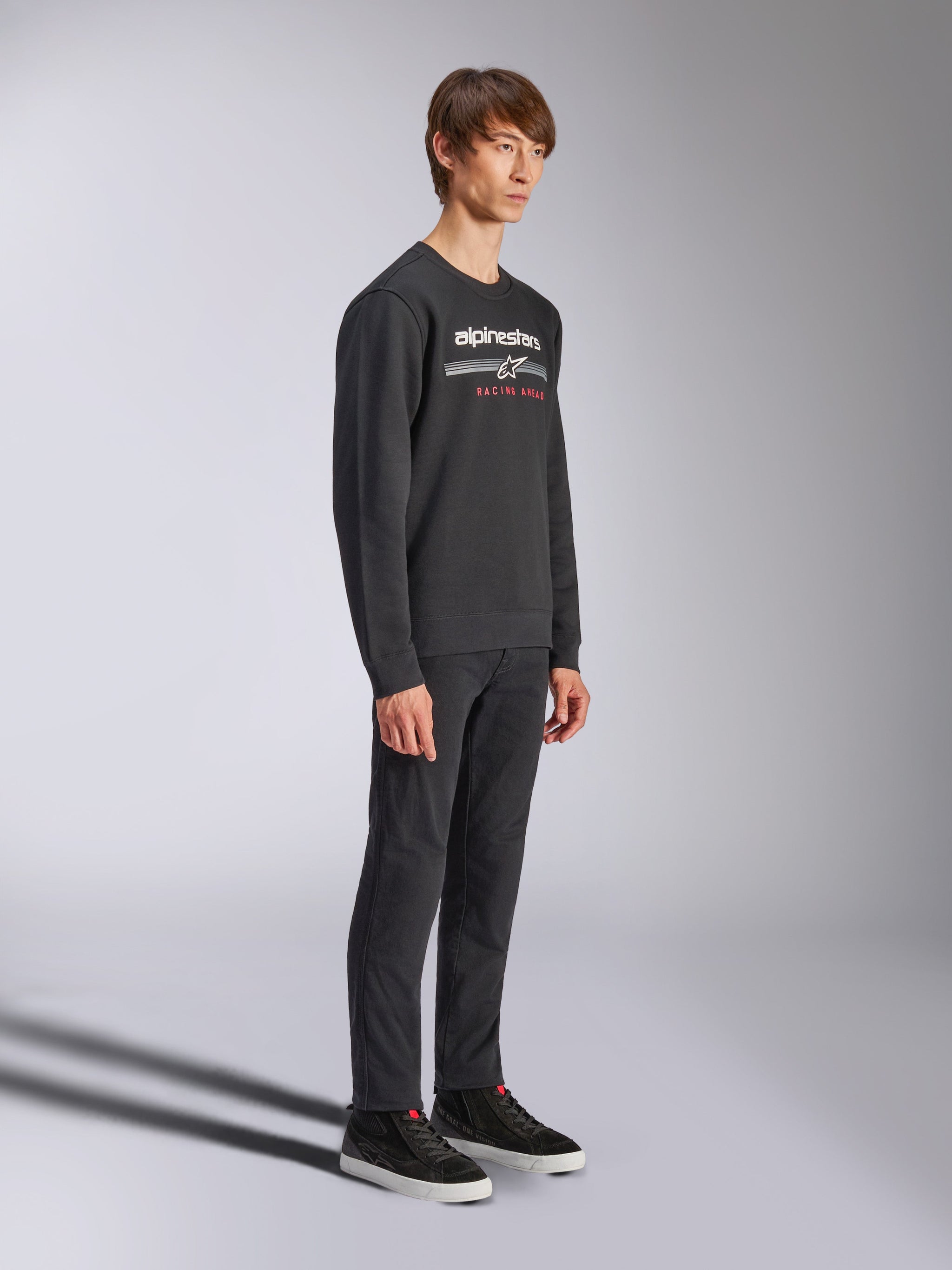 Felpa Alpinestars Bettern Crew, pullover nero a girocollo, logo Alpinestars bianco con scritta 'RACING AHEAD' in rosso sul petto, abbinata a pantaloni neri e sneakers, streetwear casual ispirato al motorsport