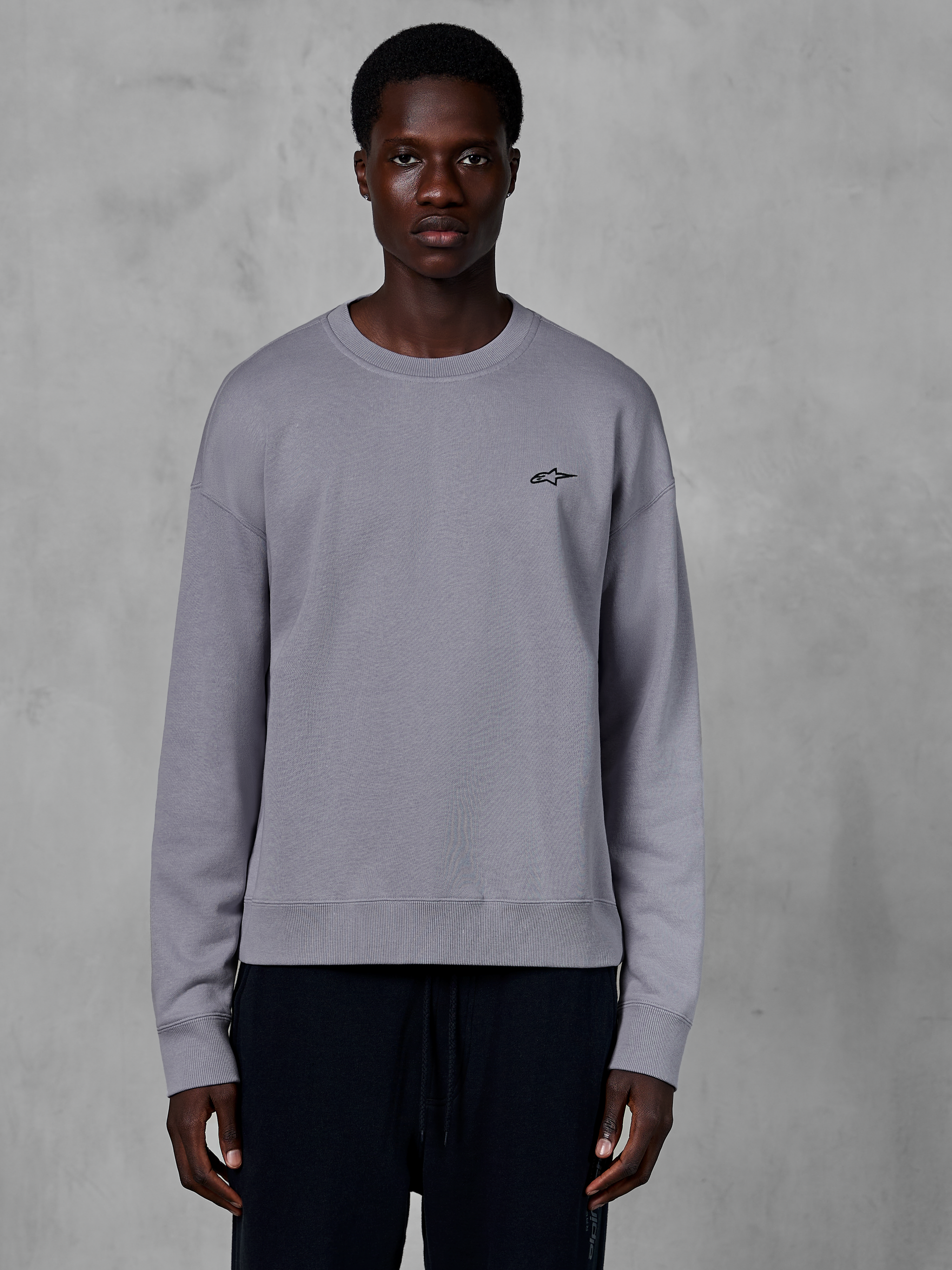 Alpinestars Essentials Ageless Crew, felpa girocollo color argento indossata da un modello, con un piccolo logo a stella nero sul petto, vestibilità rilassata con polsini e orlo a costine, abbigliamento streetwear casual motorsport