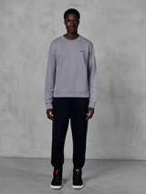 Alpinestars Essentials Ageless Crew, felpa girocollo argento, indossata da un modello con pantaloni jogger neri e sneakers nere, con un piccolo logo Alpinestars nero sul petto, streetwear casual ispirato al motorsport