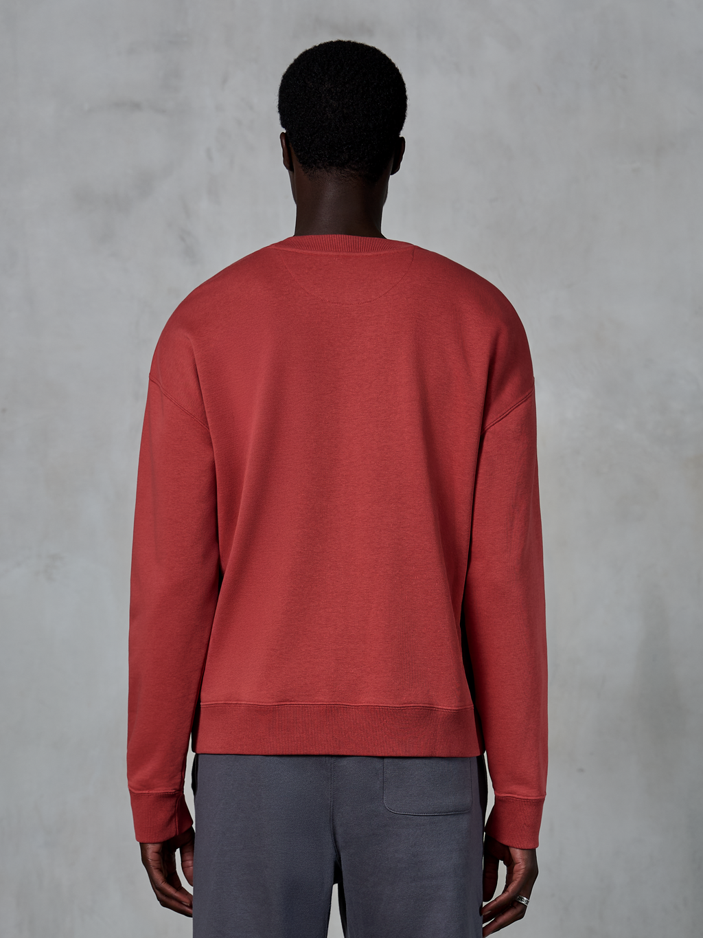 Alpinestars Essentials Ageless Crew, felpa girocollo rosso mattone, vista posteriore del modello che indossa il pullover con vestibilità rilassata, colletto e polsini a costine, streetwear casual ispirato al motorsport