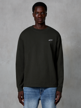 Alpinestars Essentials Ageless LS Tee, maglietta a maniche lunghe, Off Black, con un piccolo logo Alpinestars bianco sul petto, indossata da un modello con jeans blu, streetwear casual in cotone organico