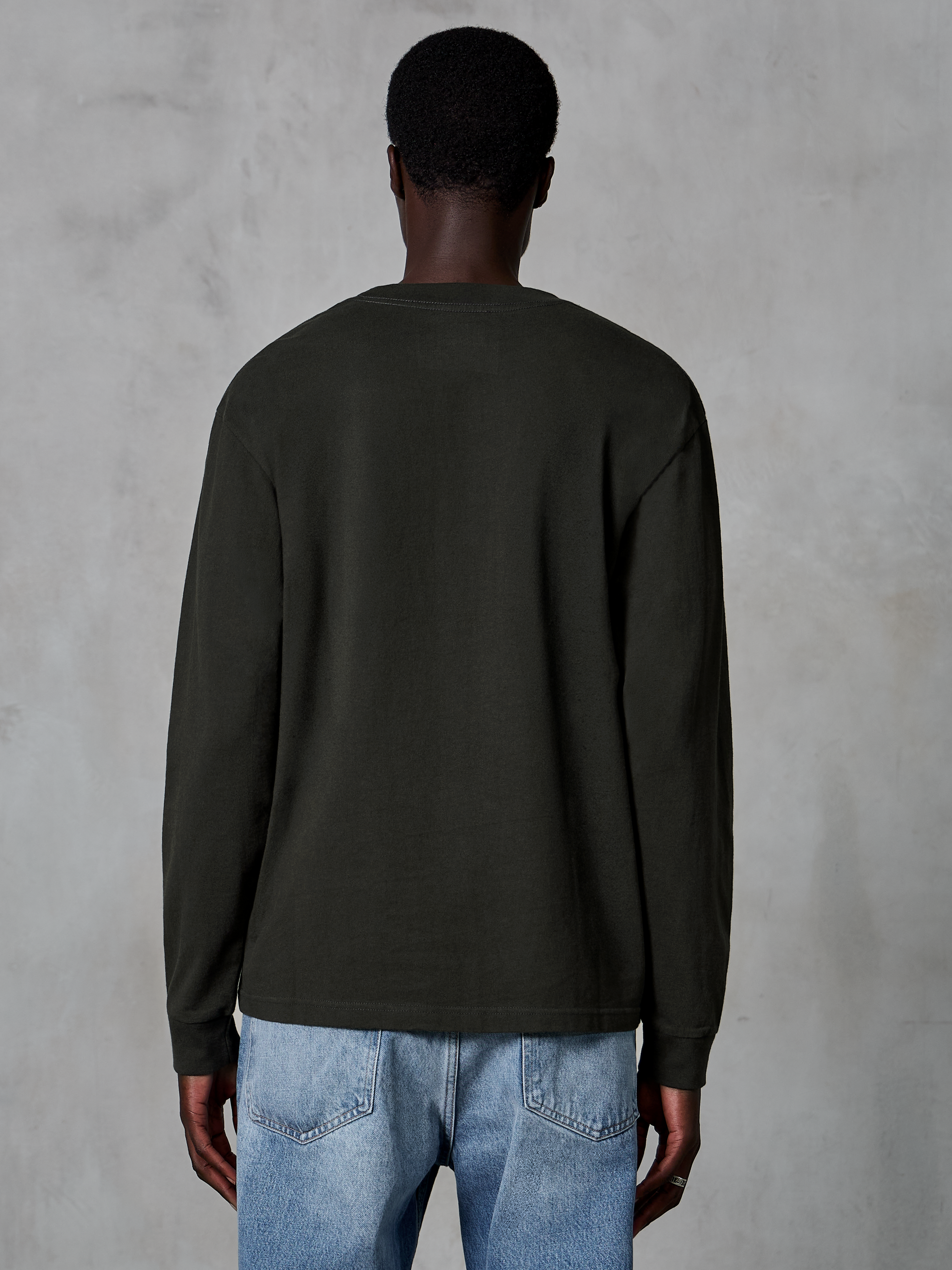 Alpinestars Essentials Ageless LS Tee, t-shirt a maniche lunghe, Off Black, vista posteriore con design pulito e vestibilità rilassata, indossata da un modello con jeans blu, streetwear casual ispirato al motorsport