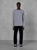 Alpinestars Essentials Ageless LS Tee, maglia a maniche lunghe, color argento, piccolo logo Alpinestars nero sul petto, jersey di cotone organico con finitura stone wash, indossata da un modello con pantaloni neri e sneakers, streetwear casual