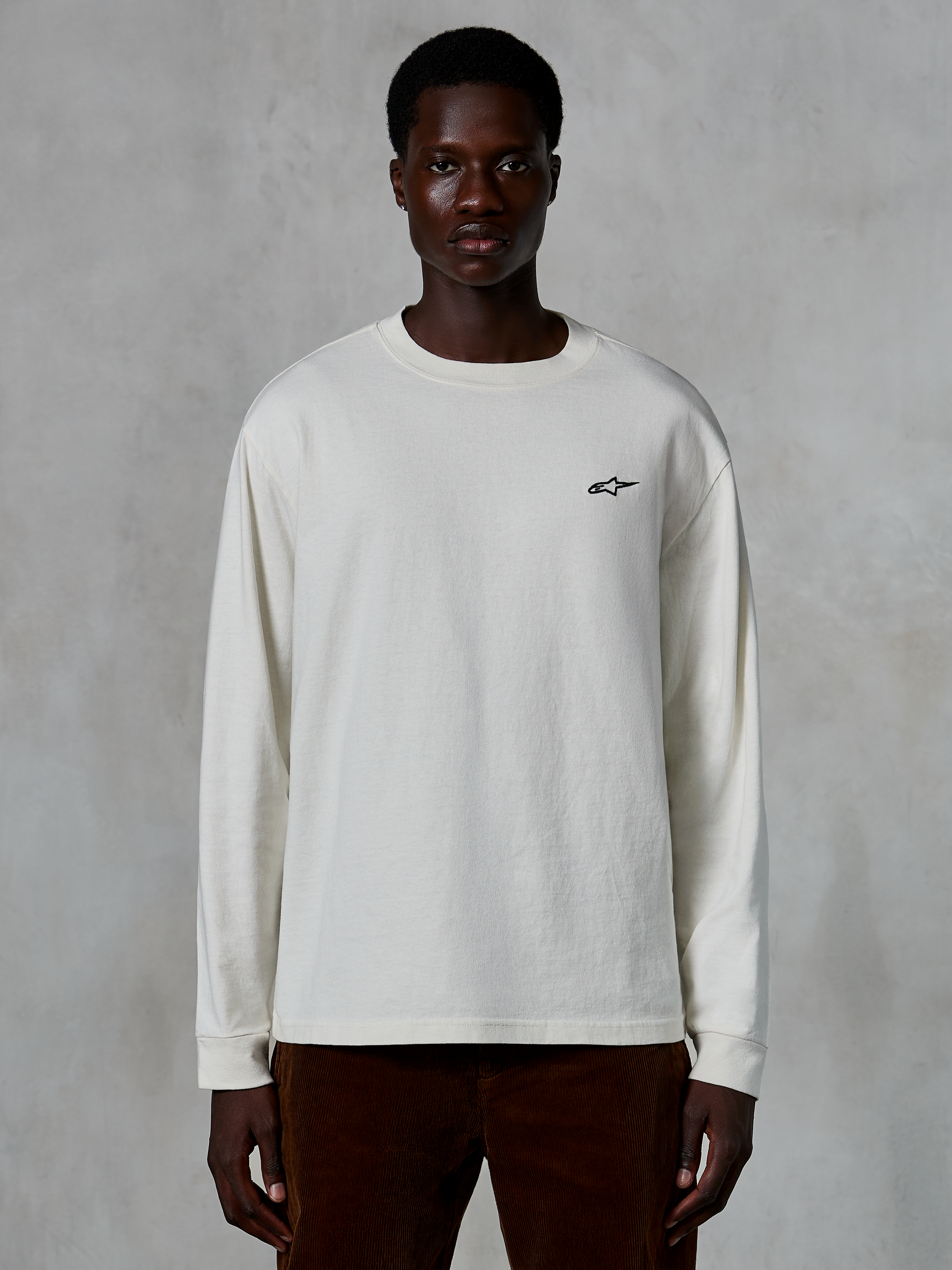 Alpinestars Essentials Ageless LS Tee, t-shirt a maniche lunghe, bianco sporco, piccolo logo a stella nero sul petto, streetwear casual, vestibilità rilassata, indossata da un modello