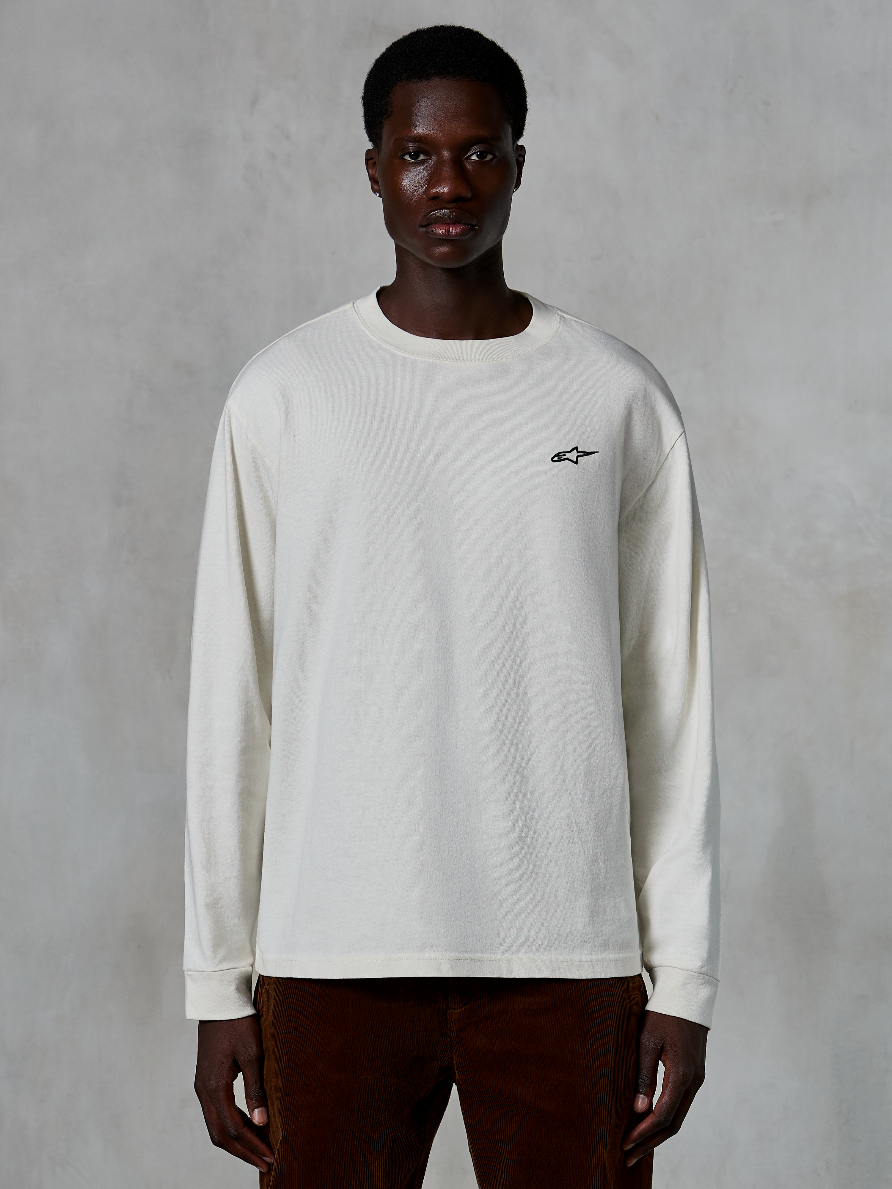 Alpinestars Essentials Ageless LS Tee, t-shirt a maniche lunghe, bianco sporco, piccolo logo a stella nero sul petto, streetwear casual, vestibilità rilassata, indossata da un modello