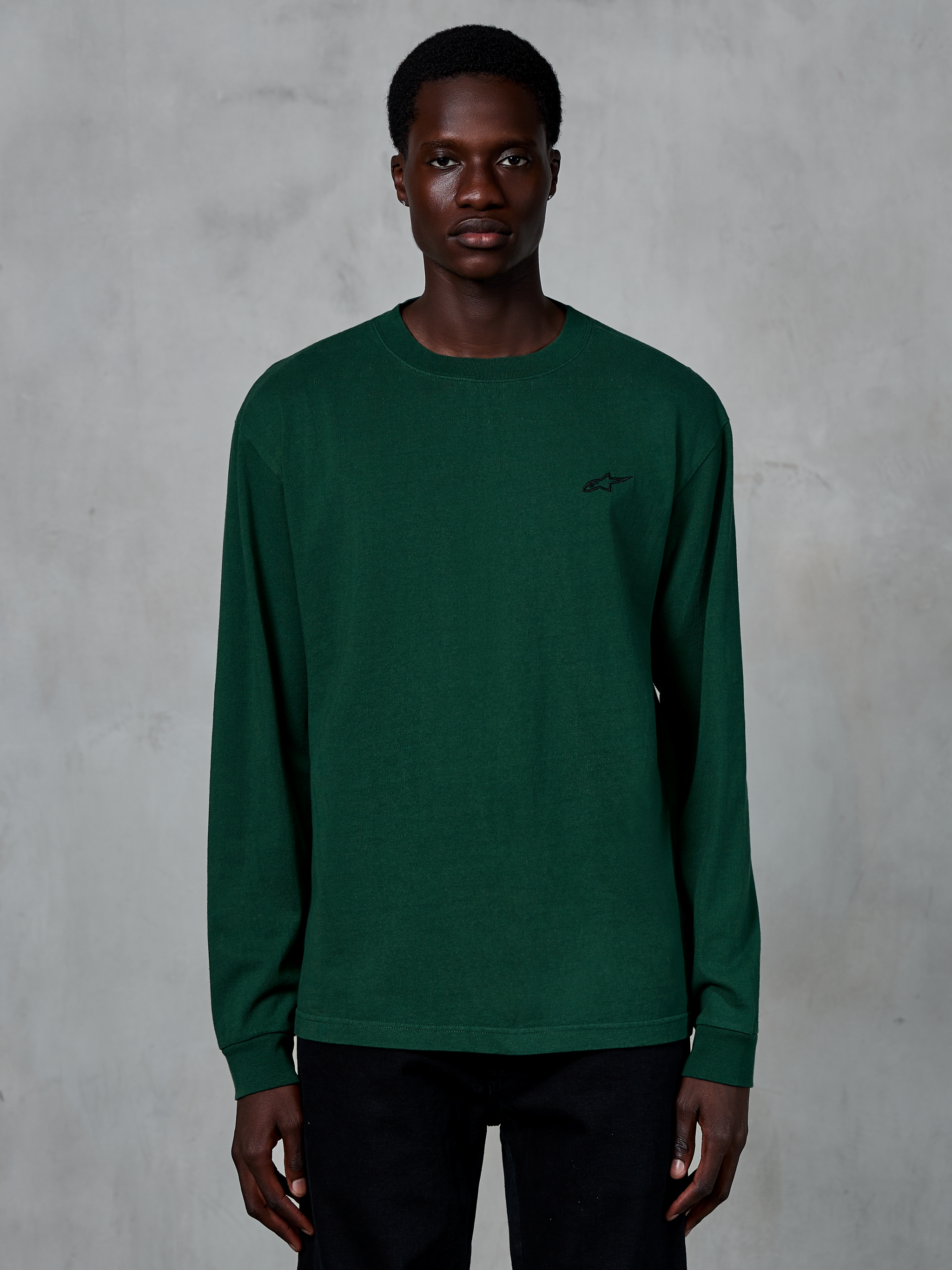 Alpinestars Essentials Ageless LS Tee, maglia a maniche lunghe, verde pino, indossata da un modello, piccolo logo nero sul petto, streetwear casual, 100% cotone organico con finitura stone wash