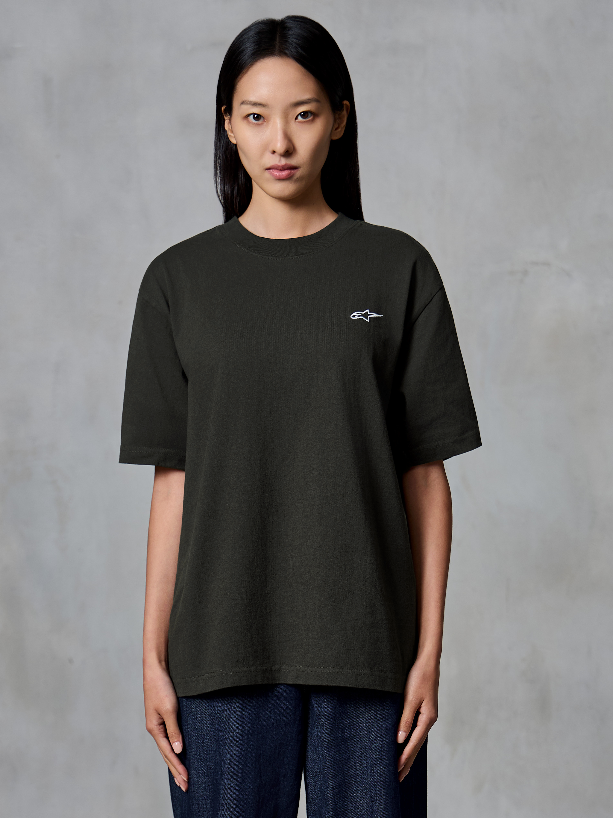Alpinestars Essentials Ageless SS Tee, maglietta a maniche corte, Off Black, indossata da una modella, vestibilità rilassata con un piccolo logo Alpinestars bianco sul lato sinistro del petto, abbigliamento lifestyle casual