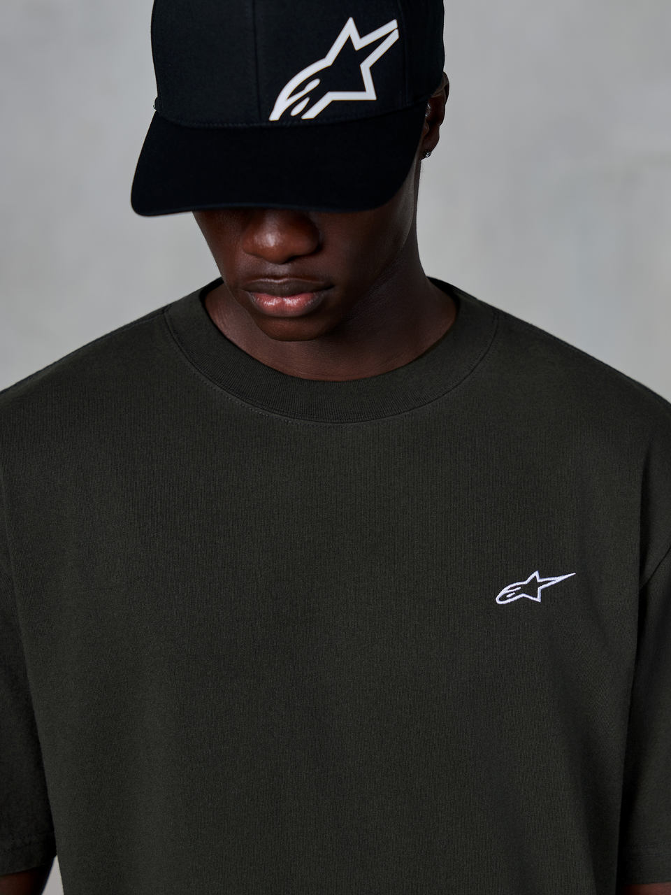 Alpinestars Essentials Ageless SS Tee, t-shirt a maniche corte, nero, con un piccolo logo Alpinestars bianco sul petto, indossata con un cappellino da baseball nero con logo, stile casual motorsport streetwear