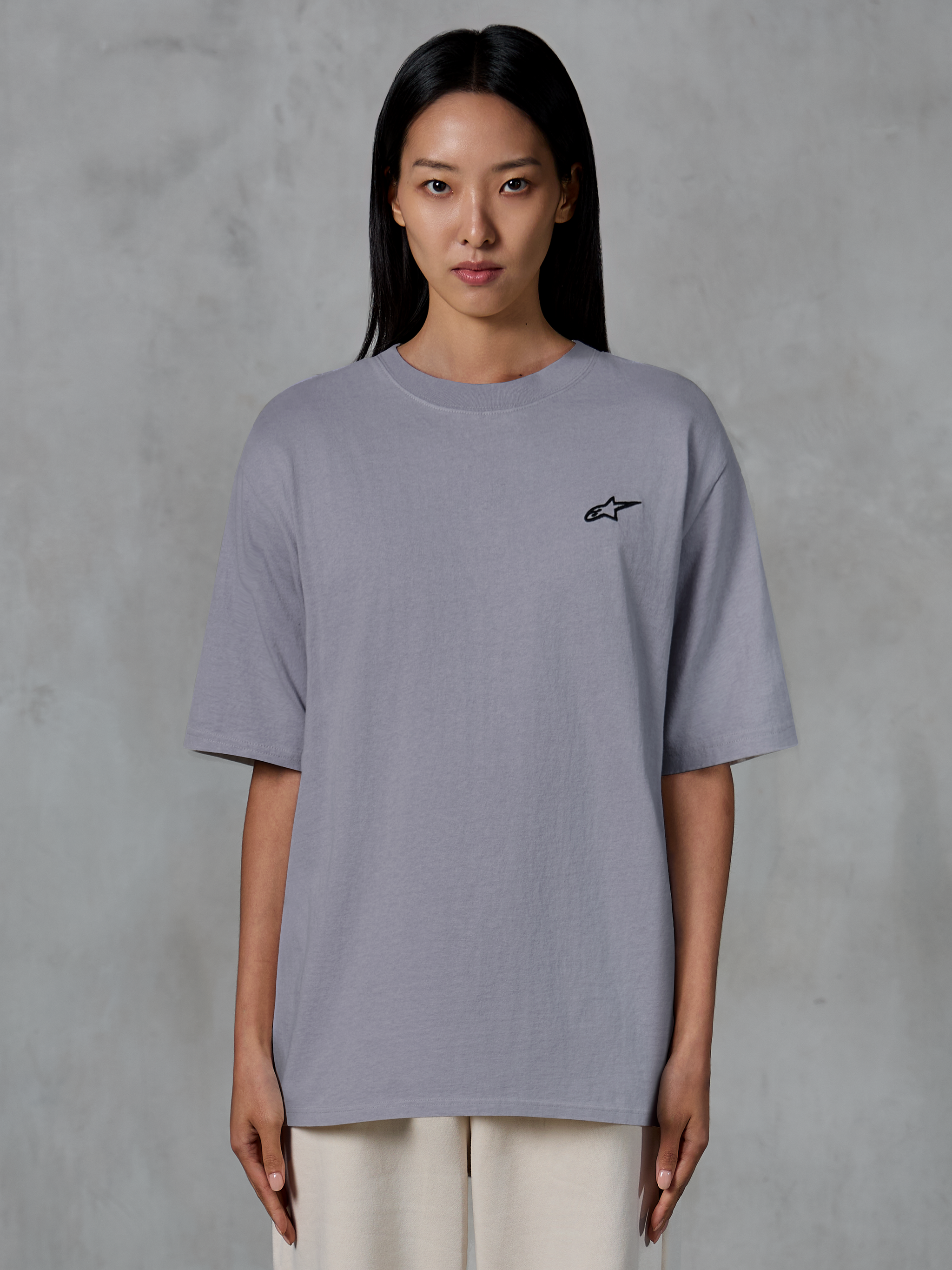 Alpinestars Essentials Ageless SS Tee, maglietta a maniche corte, Silver, con un piccolo logo Alpinestars nero sul petto, vestibilità rilassata e contemporanea, in cotone organico, abbigliamento casual lifestyle streetwear indossato da una modella