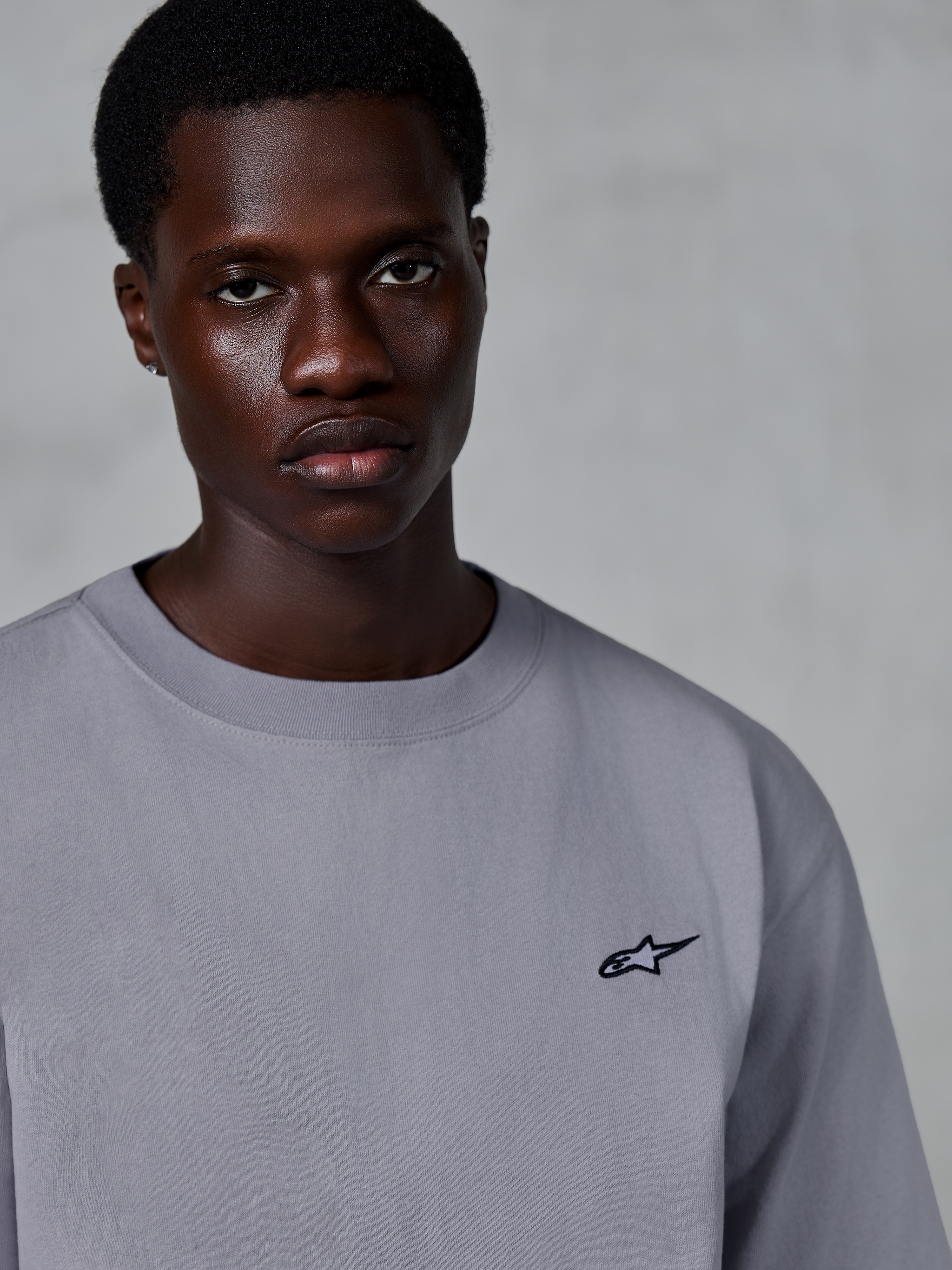 Alpinestars Essentials Ageless SS Tee, maglietta a maniche corte, argento, con un piccolo logo a stella nero sul petto, indossata da un modello, abbigliamento casual lifestyle streetwear