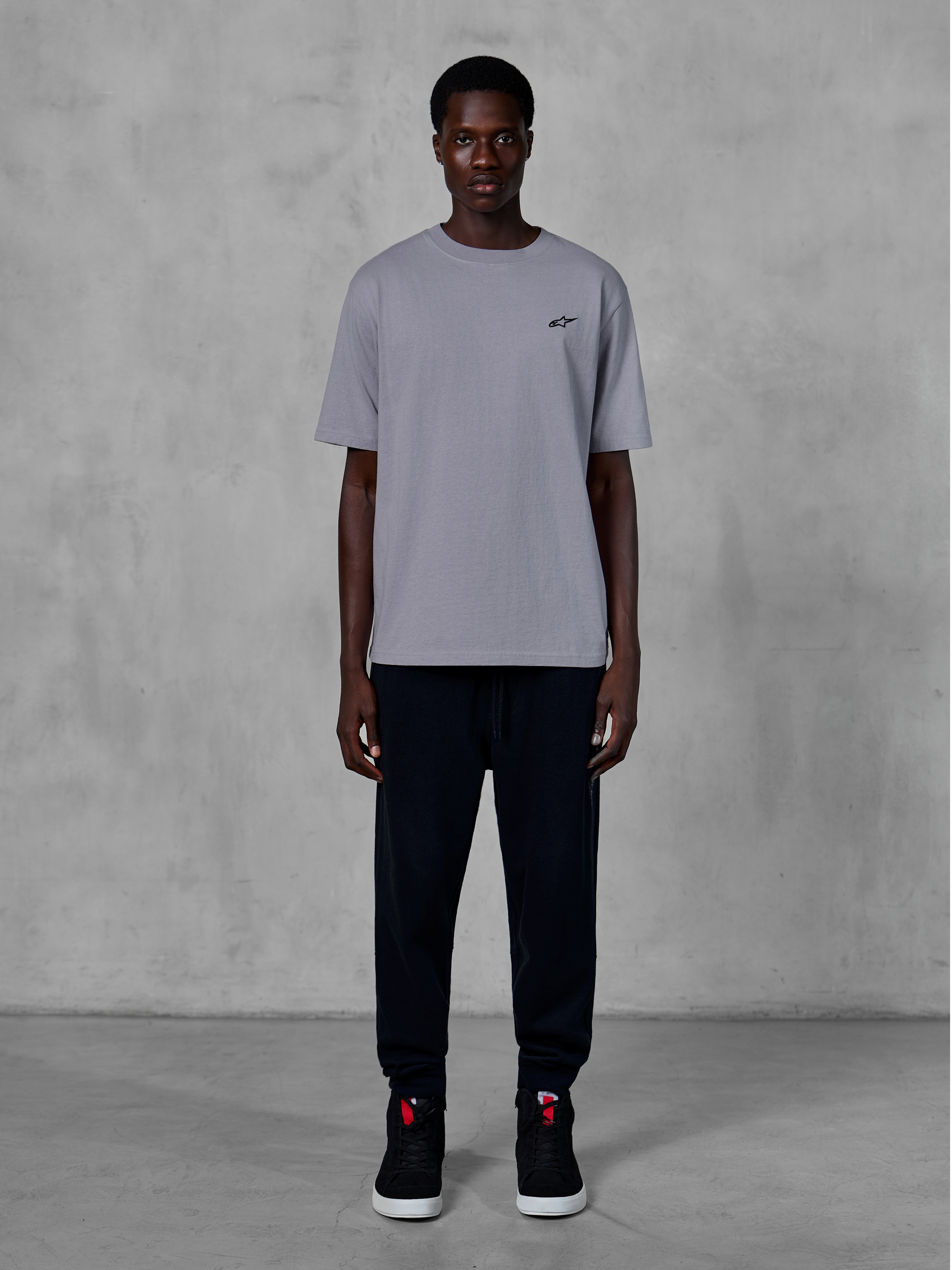 T-shirt Alpinestars Essentials Ageless SS, maglietta a maniche corte, Silver, con un piccolo logo nero sul petto, abbinata a joggers e sneakers neri, streetwear casual ispirato al motorsport