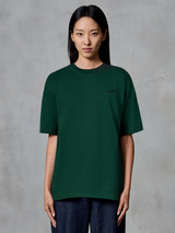 Alpinestars Essentials Ageless SS Tee, t-shirt a maniche corte, verde pino, indossata da una modella, con un piccolo logo nero sul petto, vestibilità rilassata, streetwear casual in cotone biologico