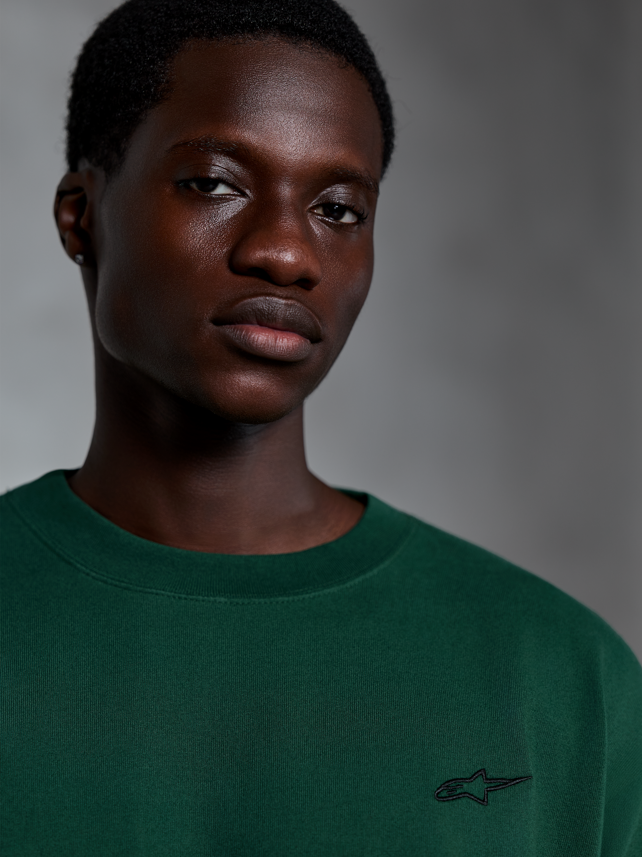 Alpinestars Essentials Ageless SS Tee, maglietta a maniche corte verde pino, primo piano di un modello che indossa una t-shirt in cotone organico verde con piccolo logo ricamato, design streetwear casual