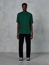 Alpinestars Essentials Ageless SS Tee, maglietta a maniche corte, verde pino, con un discreto logo nero sul petto, indossata da un modello con pantaloni neri e sneakers, streetwear casual lifestyle con vestibilità rilassata