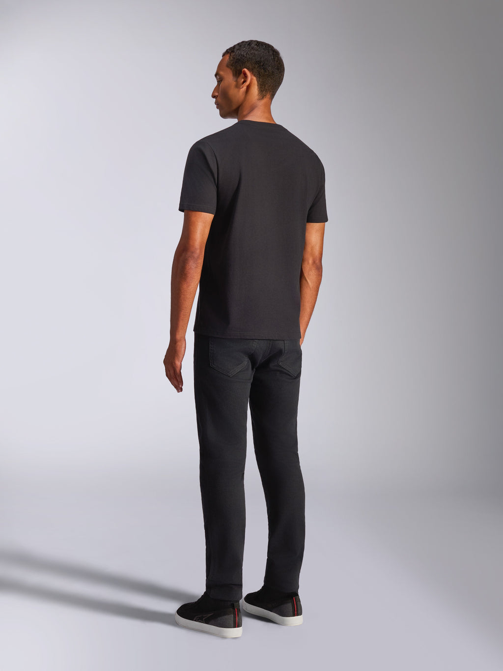 Alpinestars Shaded CSF Tee, t-shirt a maniche corte, nero, vista posteriore di un modello che indossa pantaloni neri e scarpe casual, abbigliamento motorsport lifestyle