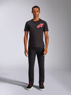 Modello che indossa la t-shirt Alpinestars Shaded CSF a maniche corte nera, con logo Astars rosso sul petto caratterizzato da stampa a gradiente in lamina inclinata, abbinata a pantaloni neri e sneakers, streetwear casual motorsport.