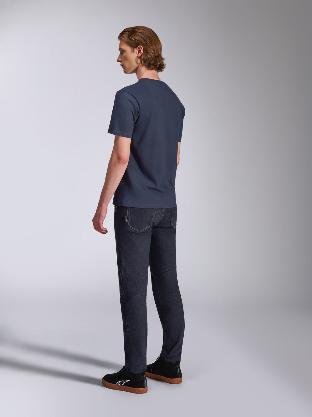 Alpinestars Fasting CSF Tee, T-shirt a maniche corte, blu navy, vista posteriore su modello, abbinata a pantaloni in denim scuro e sneakers nere, streetwear casual ispirato al motorsport