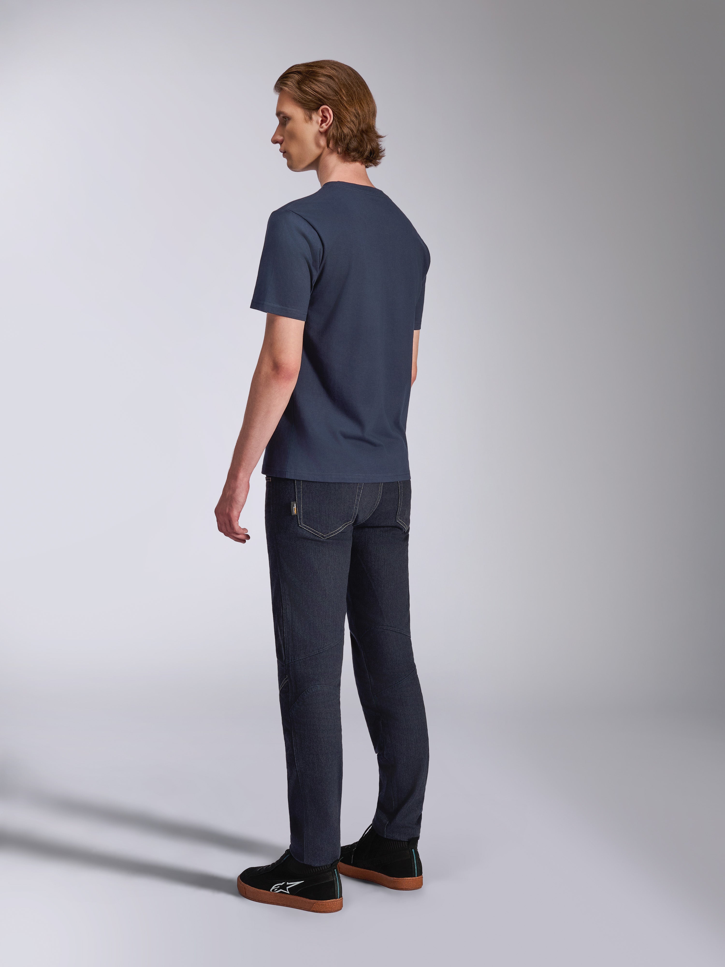 Alpinestars Fasting CSF Tee, T-shirt a maniche corte, blu navy, vista posteriore su modello, abbinata a pantaloni in denim scuro e sneakers nere, streetwear casual ispirato al motorsport