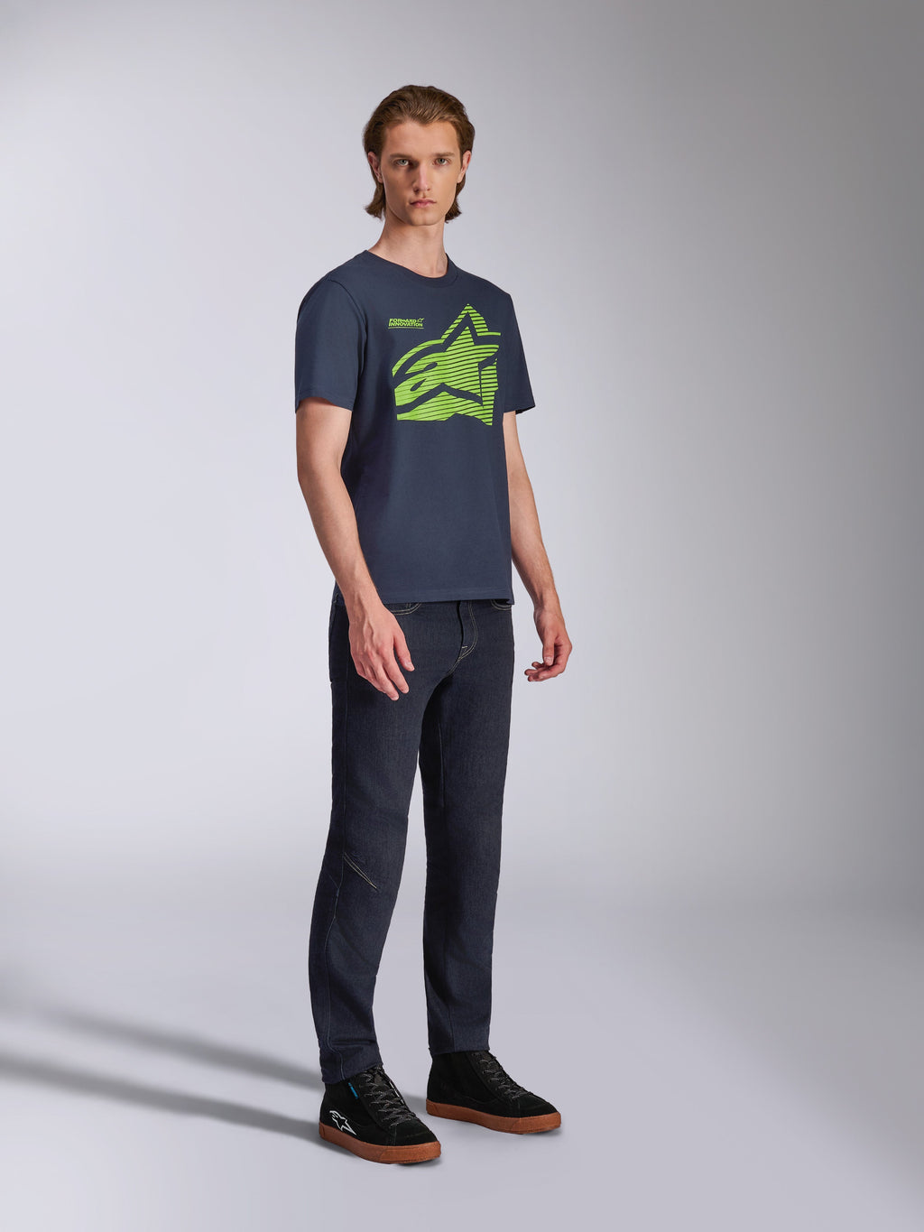 Alpinestars Fasting CSF Tee, t-shirt a maniche corte, blu navy, logo Astars geometrico verde lime, indossata con jeans scuri e sneakers nere, streetwear casual ispirato al motorsport