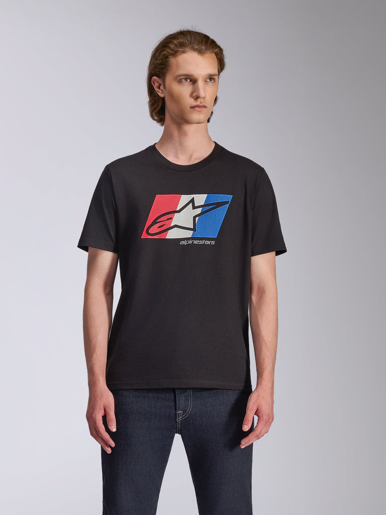Alpinestars Global CSF Tee, t-shirt a maniche corte, nero, grafica con logo Ageless rosso, bianco e blu, indossata da un modello con jeans scuri, motorsport streetwear casual