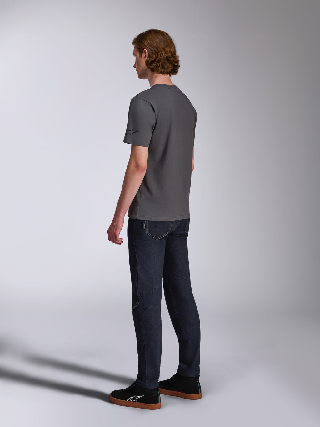 Alpinestars Waving CSF Tee, t-shirt a maniche corte, charcoal, vista posteriore su modello, piccolo logo a stella nero sulla manica, indossata con jeans in denim scuro e sneakers nere, streetwear casual motorsport