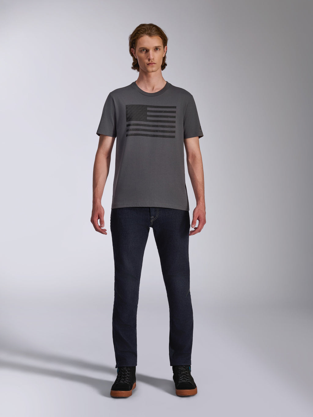 Alpinestars Waving CSF Tee, t-shirt a maniche corte, grigio antracite, grafica logo Blaze 2.0 nera stile bandiera, streetwear casual motorsport, indossata con jeans in denim scuro