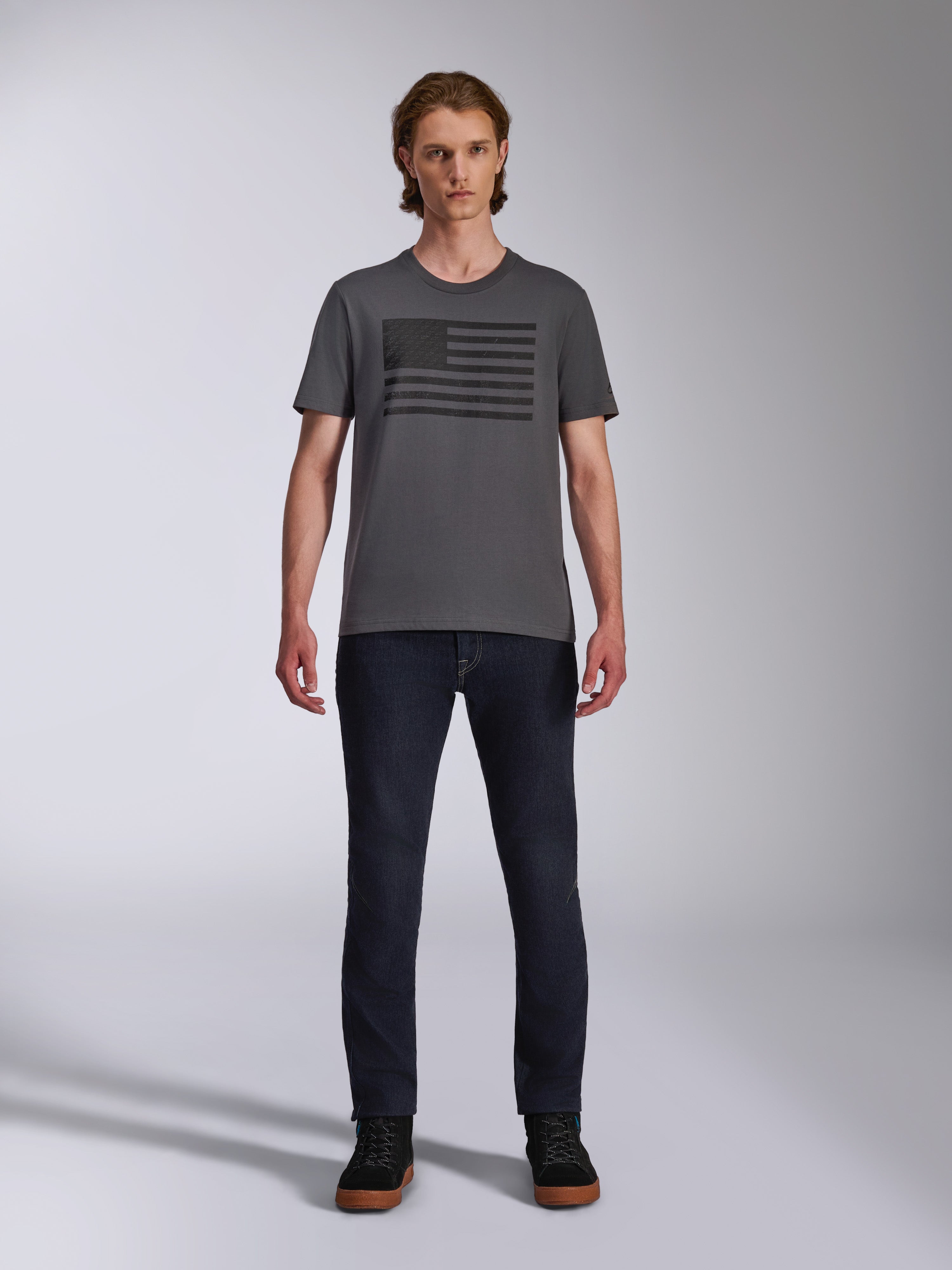Alpinestars Waving CSF Tee, t-shirt a maniche corte, grigio antracite, grafica logo Blaze 2.0 nera stile bandiera, streetwear casual motorsport, indossata con jeans in denim scuro