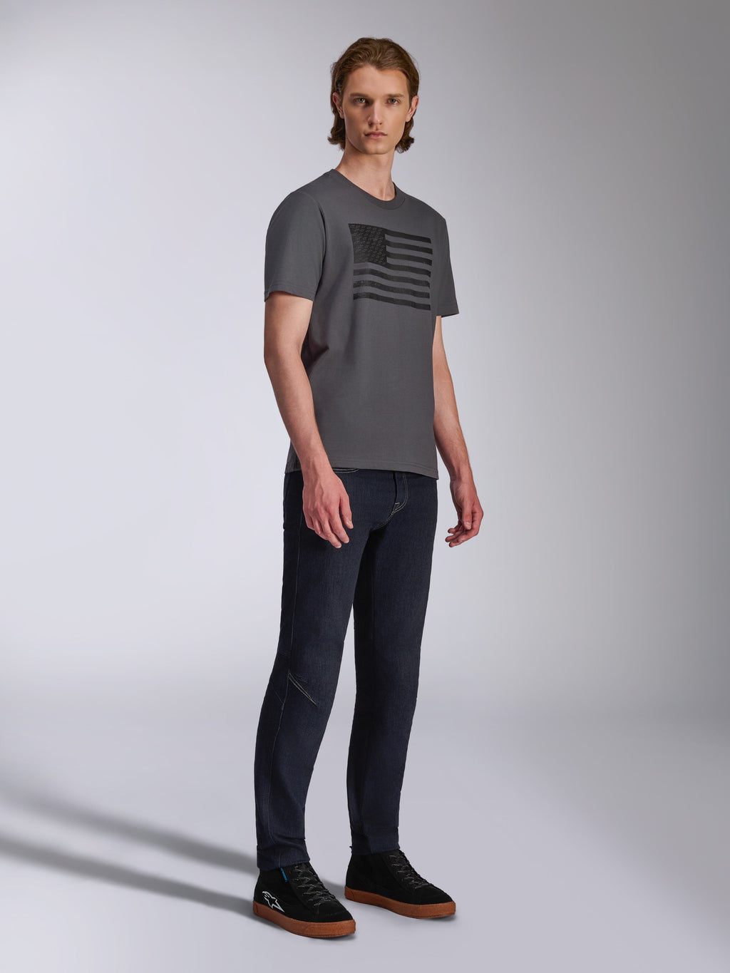 Alpinestars Waving CSF Tee, maglietta a maniche corte, antracite, grafica con bandiera ondulata nera, indossata da un modello con jeans scuri e sneakers, abbigliamento streetwear casual motorsport