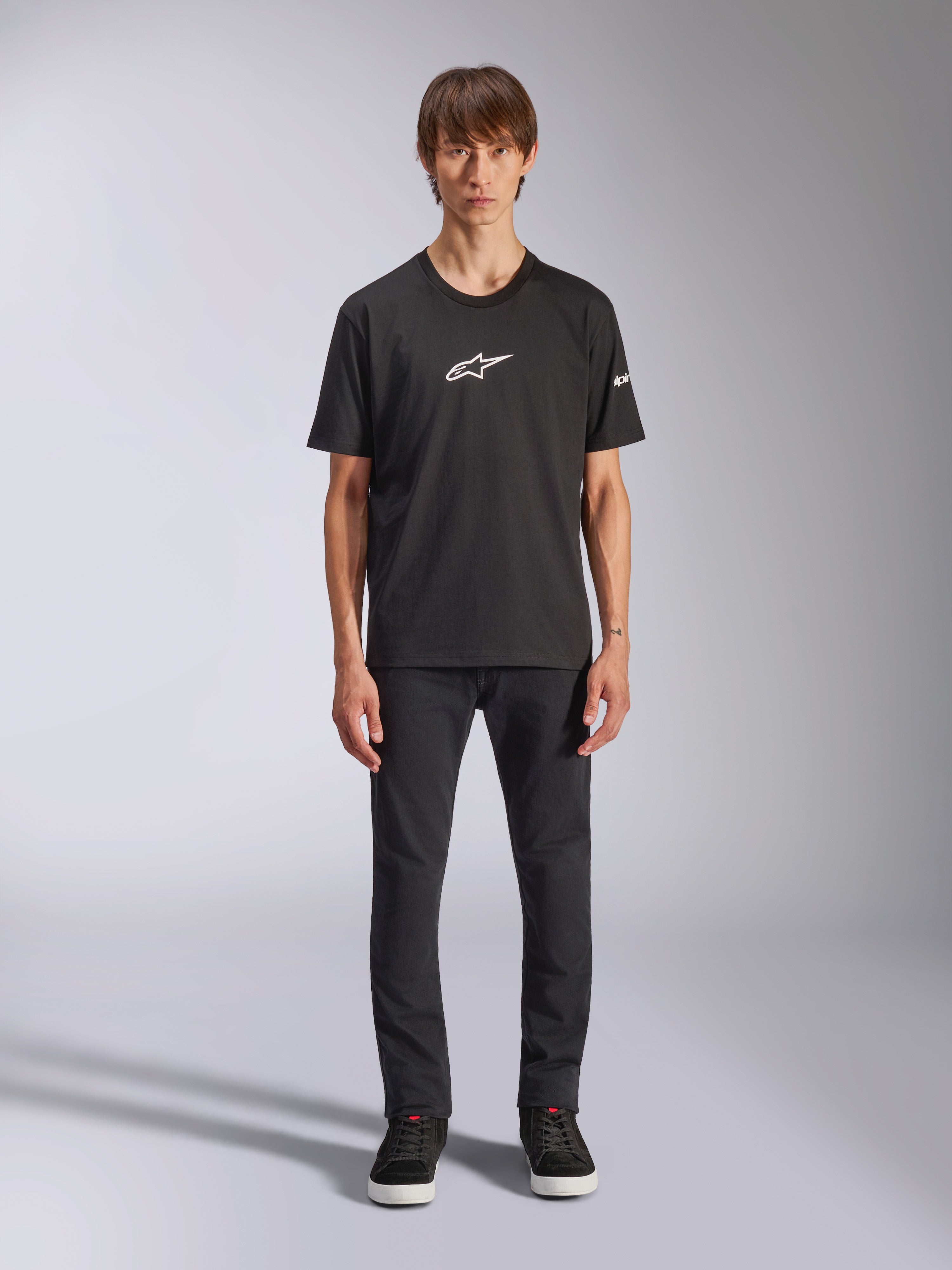 Alpinestars Frontal CSF Tee, maglietta a maniche corte, nera, logo Alpinestars bianco sul petto, indossata da un modello con pantaloni neri e scarpe nere, abbigliamento sportivo casual ad alte prestazioni