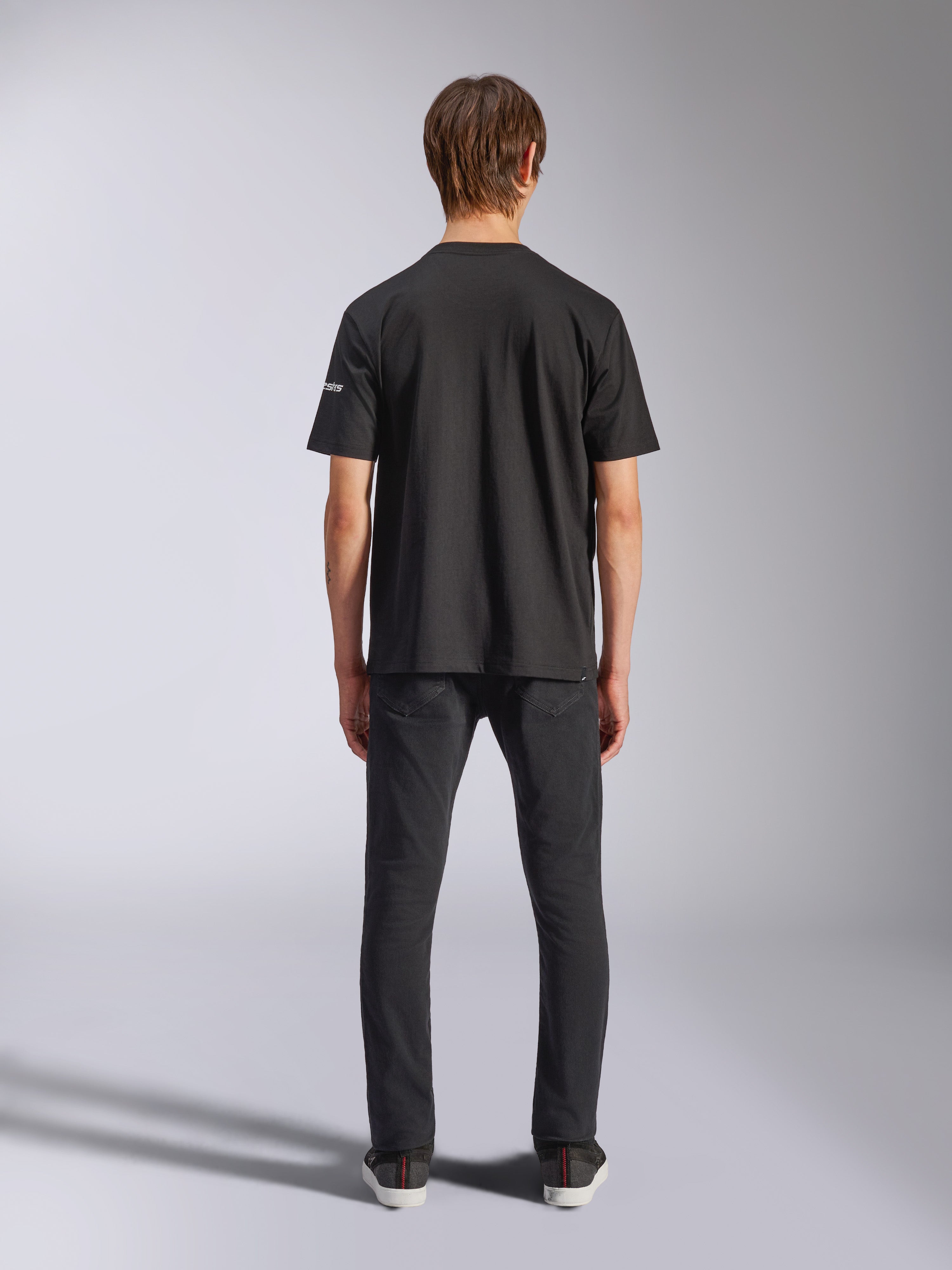 Alpinestars Frontal CSF Tee, maglietta a maniche corte, nero, vista posteriore su modello che indossa jeans neri, streetwear casual ad alte prestazioni con dettaglio del piccolo logo bianco sulla manica