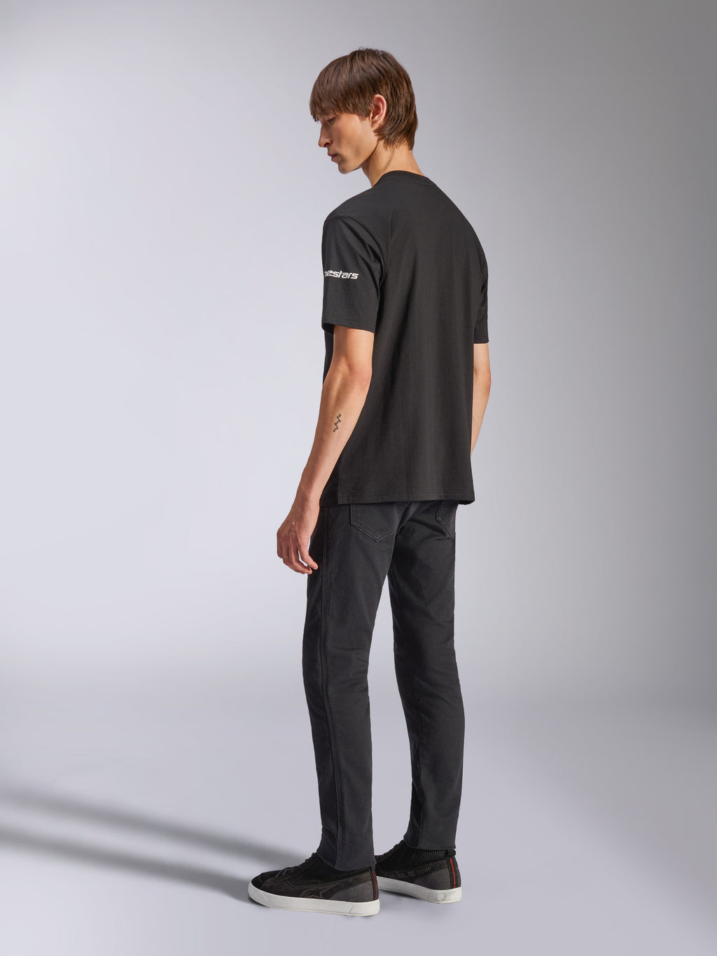 Alpinestars Frontal CSF Tee, maglietta a maniche corte, nero, marchio astars bianco sulla manica, indossata da un modello con pantaloni e scarpe neri, design casual ispirato al motorsport