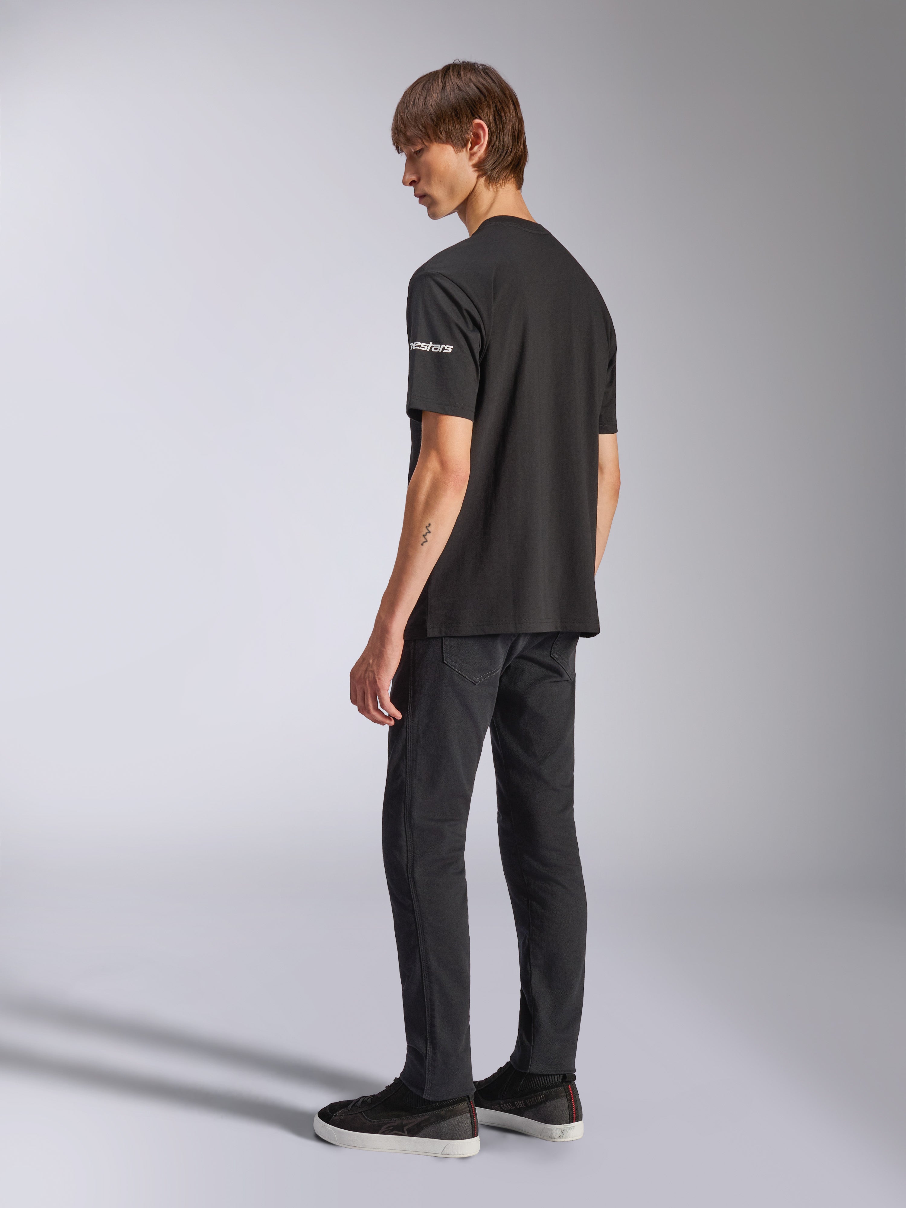 Alpinestars Frontal CSF Tee, maglietta a maniche corte, nero, marchio astars bianco sulla manica, indossata da un modello con pantaloni e scarpe neri, design casual ispirato al motorsport