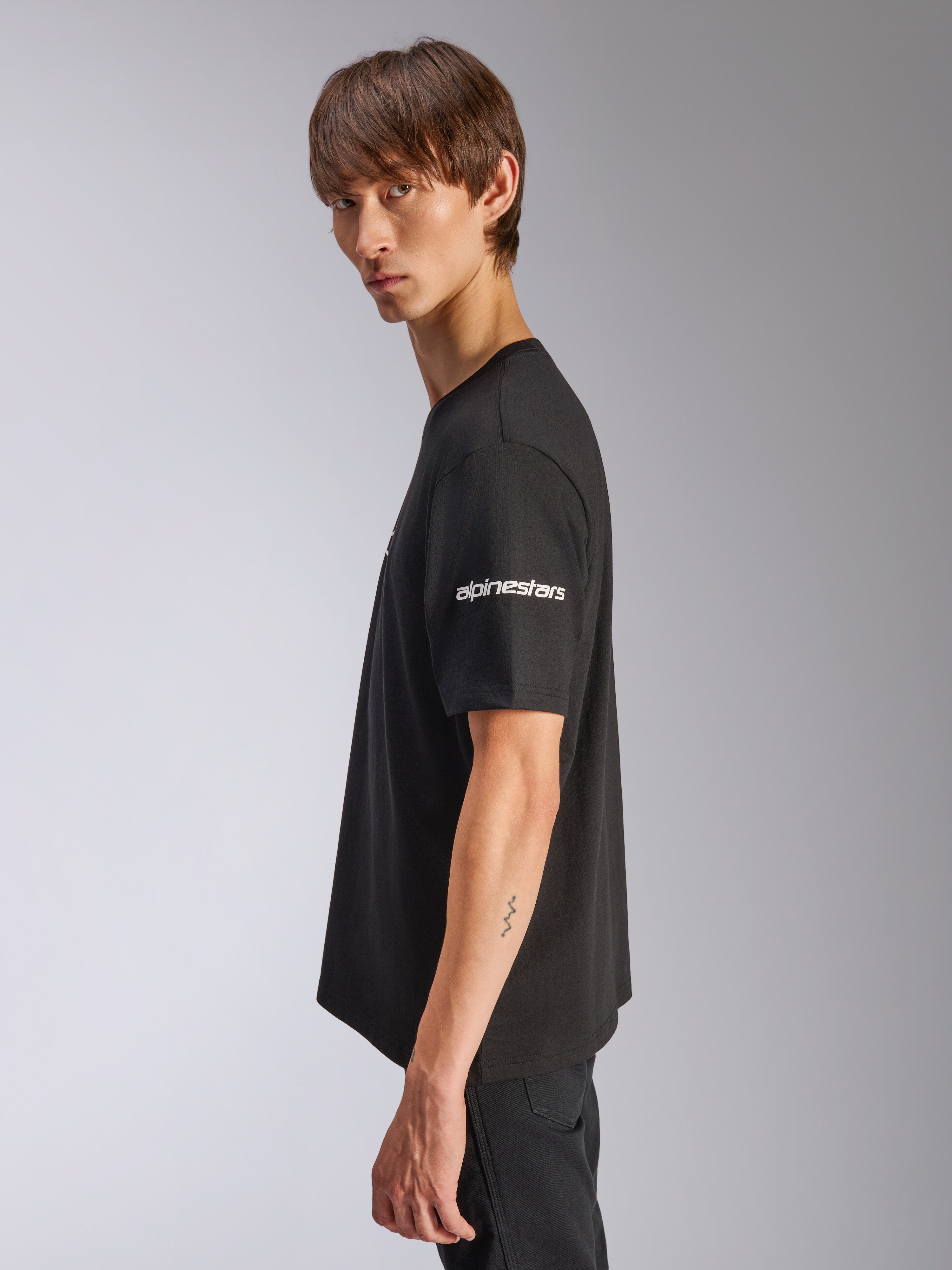 Alpinestars Frontal CSF Tee, t-shirt a maniche corte, nero, logo Alpinestars bianco sulla manica, indossata da un modello in vista di profilo, streetwear casual motorsport performance