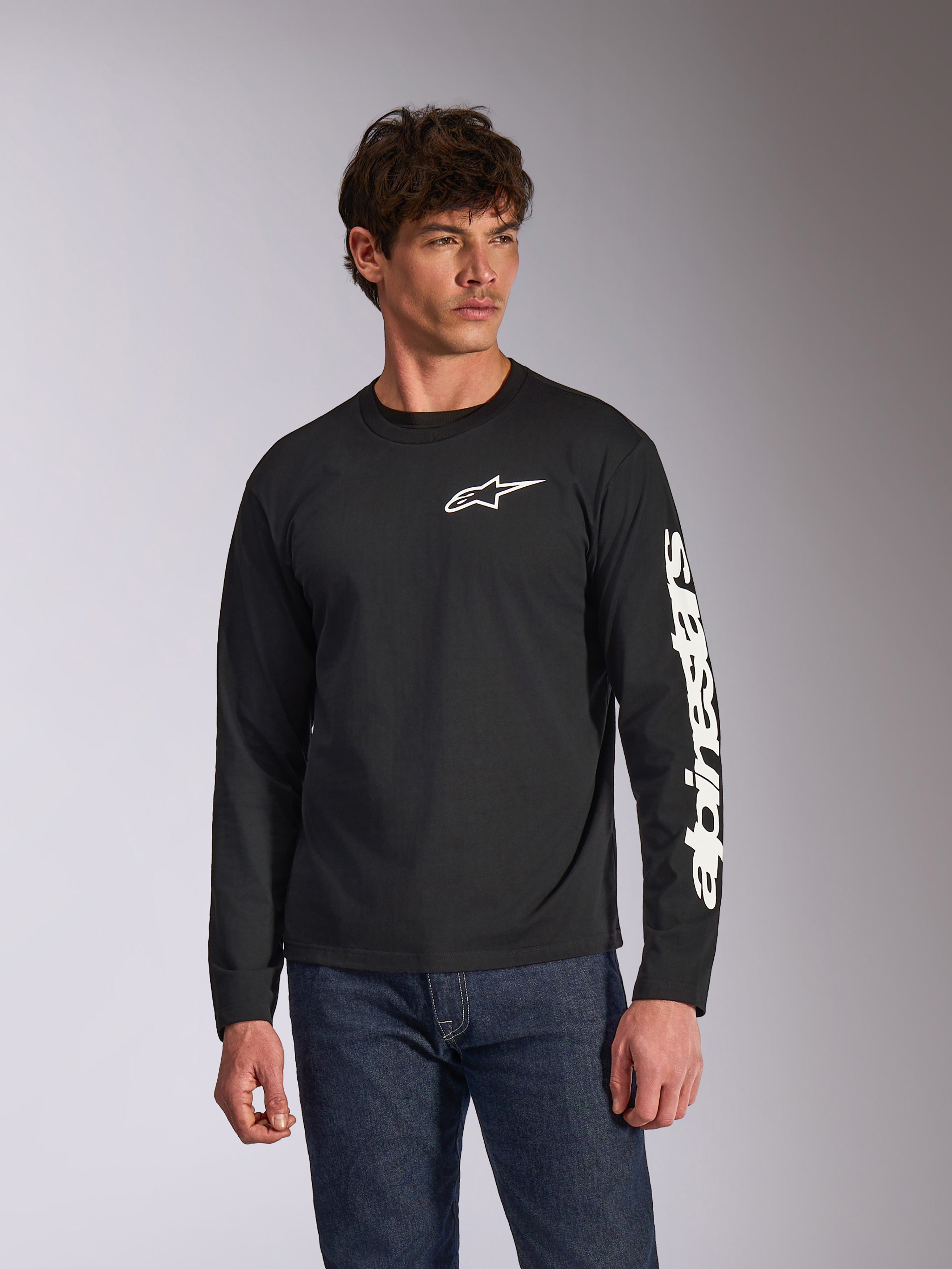 Alpinestars Trackside CSF Long Sleeve Tee, maglia a maniche lunghe nera, logo Alpinestars bianco sul petto e marchio sulla manica, indossata da un modello con jeans blu, streetwear casual motorsport