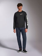 Alpinestars Trackside CSF Tee, maglietta a maniche lunghe, nero e bianco, indossata con jeans blu scuro e sneakers nere, con logo Ride 4.0 bianco sul petto e scritta Alpinestars sulla manica, streetwear casual ispirato al motorsport