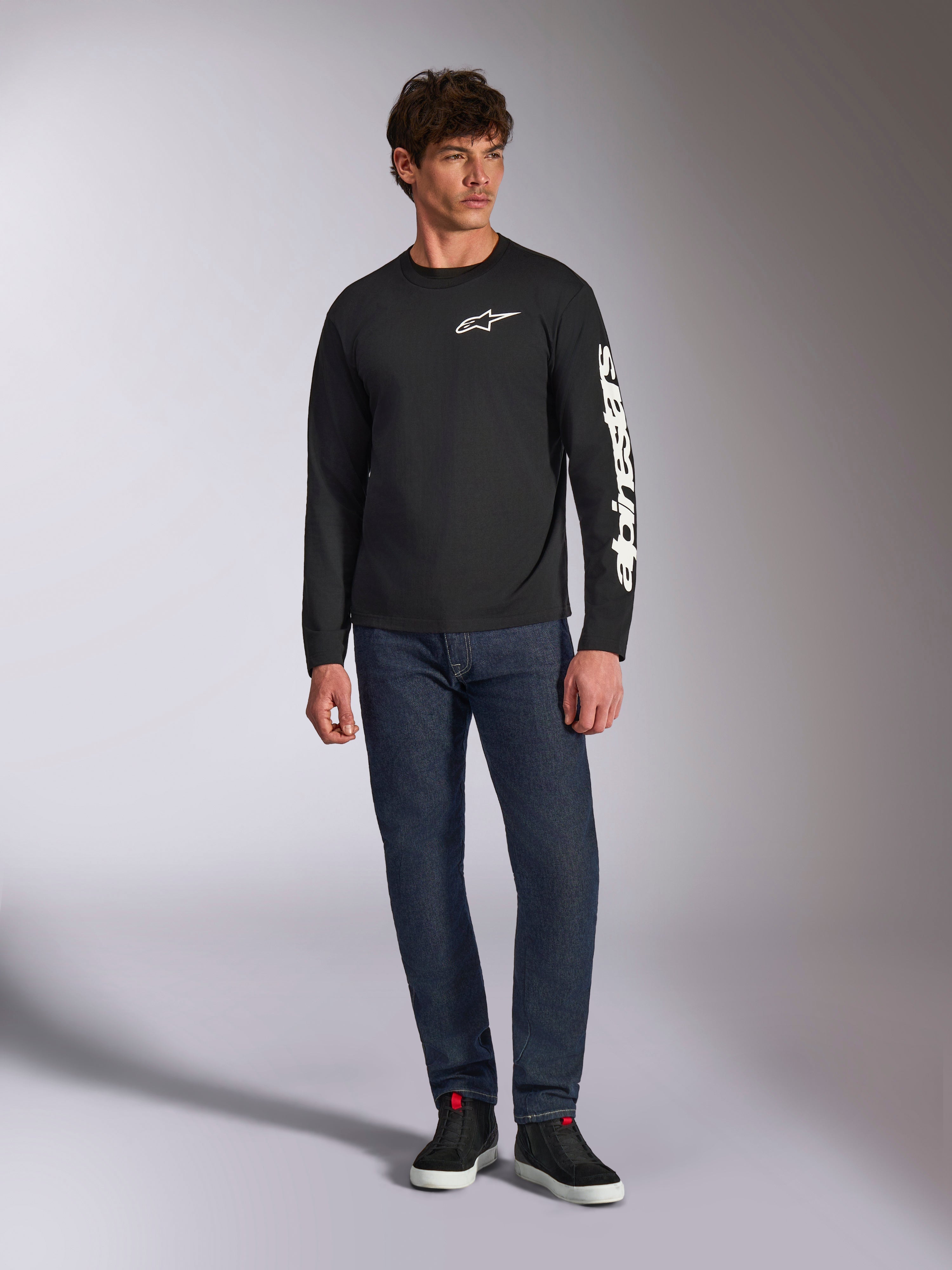 Alpinestars Trackside CSF Tee, maglietta a maniche lunghe, nero e bianco, indossata con jeans blu scuro e sneakers nere, con logo Ride 4.0 bianco sul petto e scritta Alpinestars sulla manica, streetwear casual ispirato al motorsport