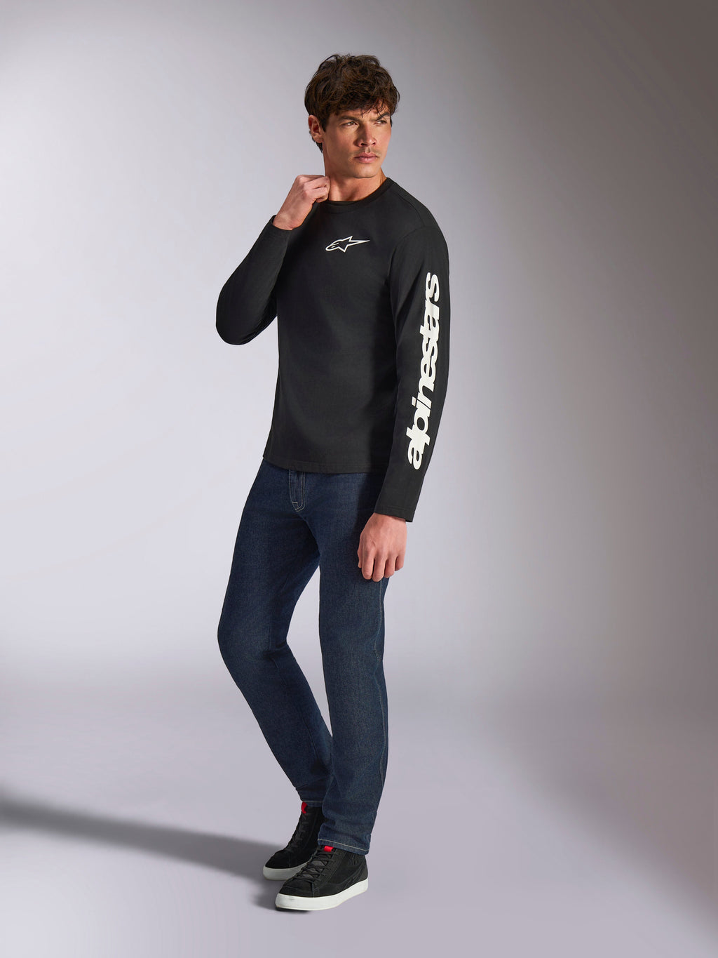 Alpinestars Trackside CSF Tee, maglia a maniche lunghe, nera, branding Alpinestars bianco verticale sulla manica e logo sul petto, indossata da un modello con jeans blu scuro e sneakers, streetwear casual motorsport