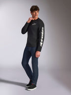 Alpinestars Trackside CSF Tee, maglia a maniche lunghe, nera, branding Alpinestars bianco verticale sulla manica e logo sul petto, indossata da un modello con jeans blu scuro e sneakers, streetwear casual motorsport