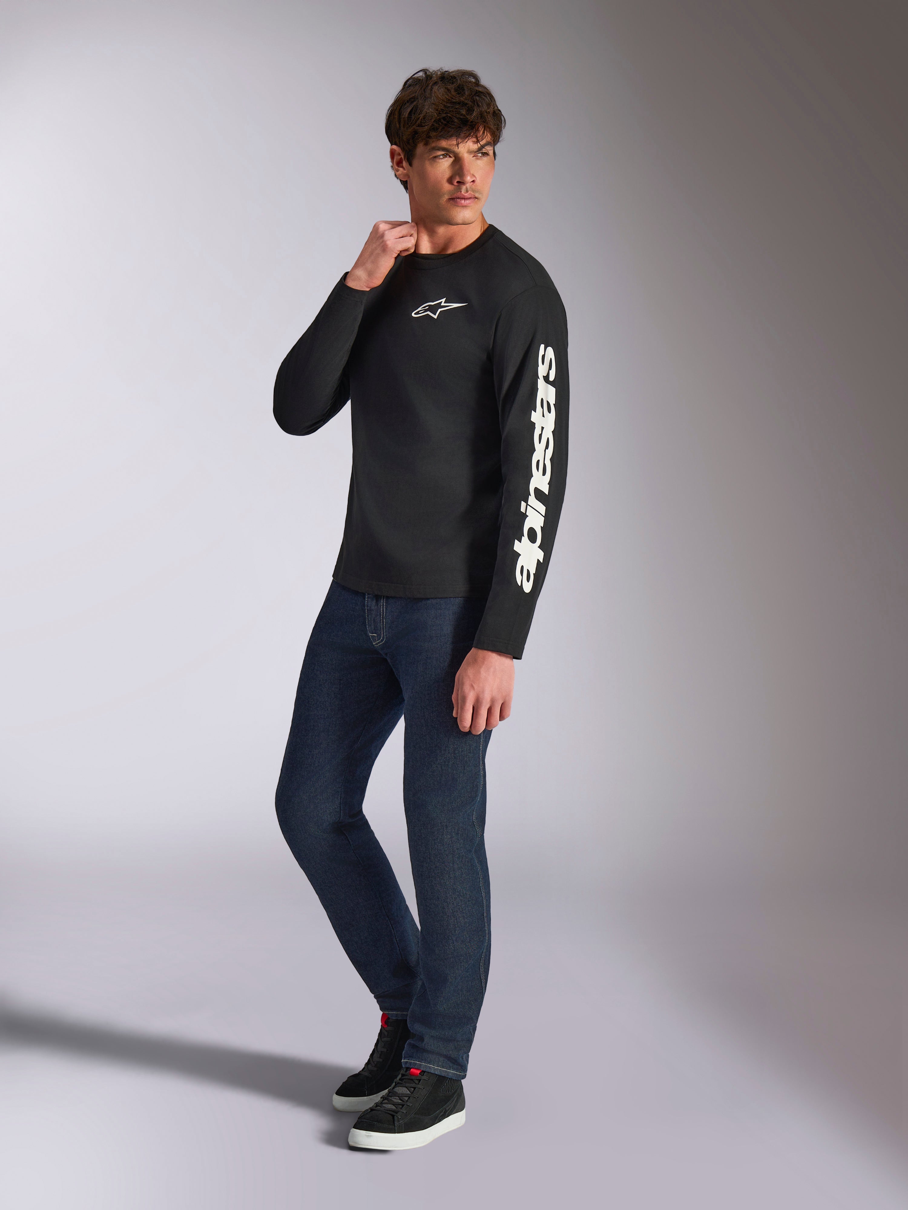 Alpinestars Trackside CSF Tee, maglia a maniche lunghe, nera, branding Alpinestars bianco verticale sulla manica e logo sul petto, indossata da un modello con jeans blu scuro e sneakers, streetwear casual motorsport