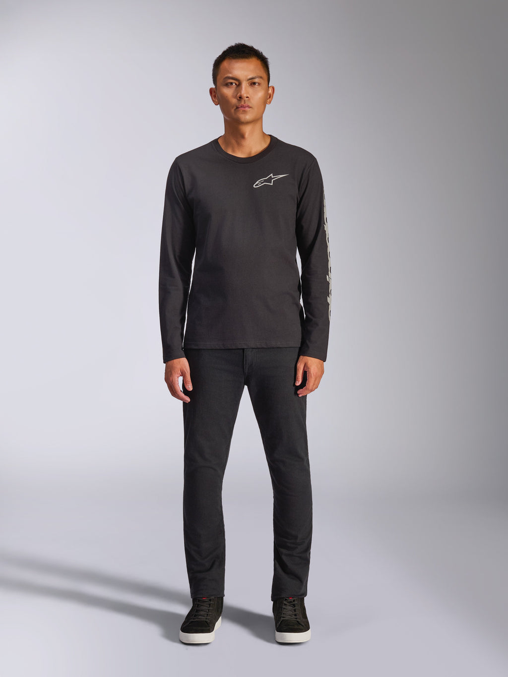 Alpinestars Trackside CSF Tee, maglia a maniche lunghe, nera, logo Alpinestars bianco sul petto e branding grafico sulla manica, indossata con pantaloni neri e sneakers, streetwear casual ispirato al motorsport