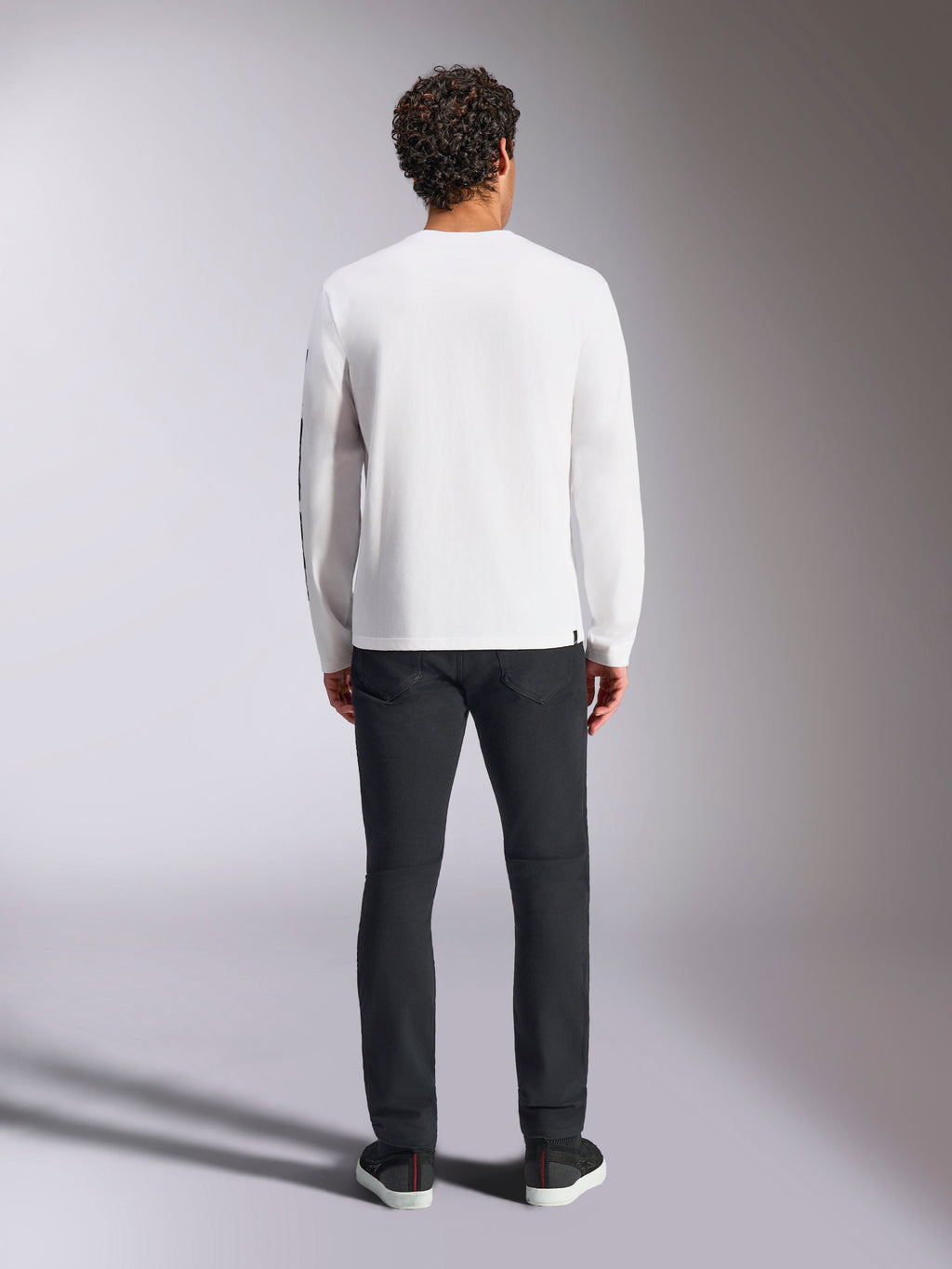 Alpinestars Trackside CSF Tee - Manica Lunga, bianca, vista posteriore della maglietta a maniche lunghe, indossata con pantaloni neri e sneakers, caratterizzata da una piccola etichetta nera sull'orlo, streetwear casual di ispirazione motorsport