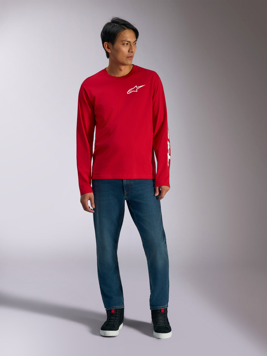 Alpinestars Trackside CSF Tee, maglia a maniche lunghe, rossa con logo Alpinestars bianco, foto lifestyle indossata con jeans blu e sneakers nere, abbigliamento sportivo casual ispirato al motorsport