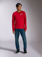 Alpinestars Trackside CSF Tee, maglia a maniche lunghe, rossa con logo Alpinestars bianco, foto lifestyle indossata con jeans blu e sneakers nere, abbigliamento sportivo casual ispirato al motorsport