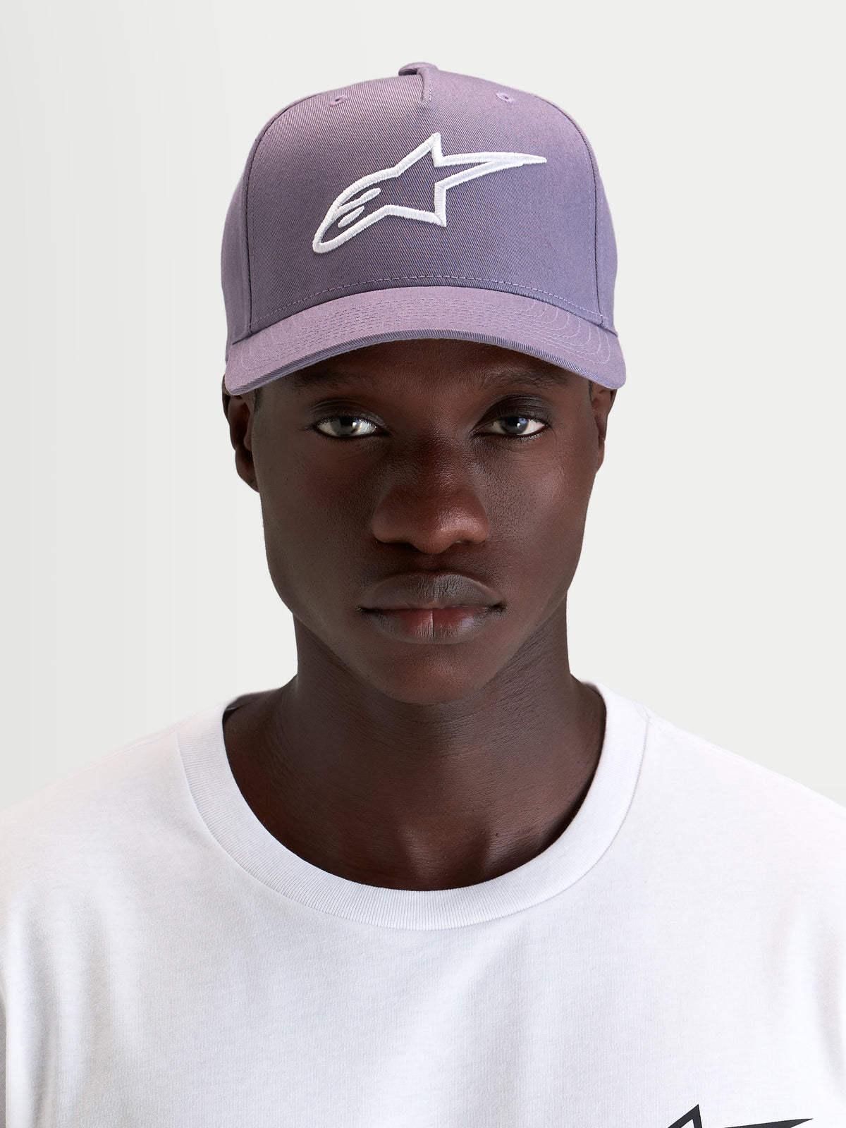 Alpinestars Cappello Ageless Snapback, cappello sportswear con visiera curva, viola e bianco, indossato da un modello che mostra il logo Astars ricamato in 3D sul davanti e il profilo in twill strutturato