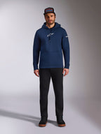 Modello indossa la felpa con cappuccio Alpinestars Frontal in colore Navy, felpa in pile con logo Astars bianco sul petto e logo con scritta sulla manica, con tasca a marsupio e cappuccio con cordino, abbinata a pantaloni neri e cappellino con logo, streetwear casual motorsport