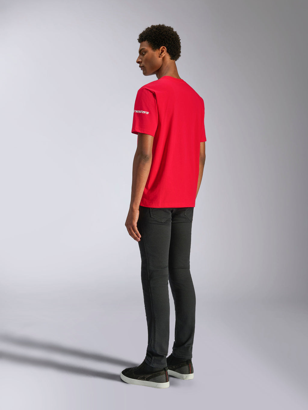 Alpinestars Frontal CSF Tee, maglietta a maniche corte, rosso, vista posteriore su modello, con logo bianco sulla manica, abbinata a pantaloni neri, streetwear casual ad alte prestazioni