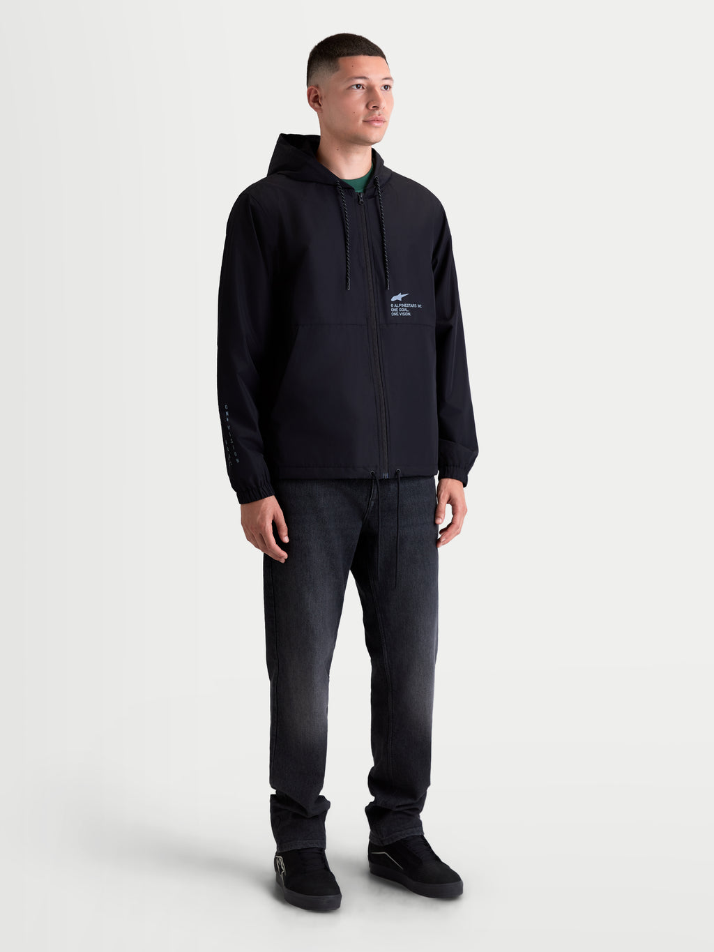 Alpinestars Giacca frangivento Speeder Resolve, giacca frangivento leggera da uomo per sportswear e uso urbano, nera, dotata di cappuccio regolabile con coulisse, fodera interna in rete e loghi d'ispirazione motorsport su petto e manica, mostrata su un modello.