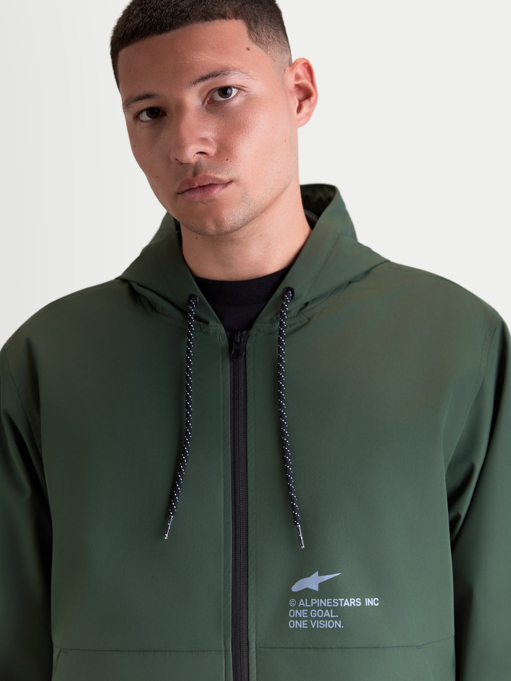 Alpinestars Giacca frangivento Speeder Resolve, giacca con cappuccio leggera e sportswear, verde, dotata di cappuccio regolabile con coulisse puntinate e logo Alpinestars sul petto, indossata da un modello uomo.
