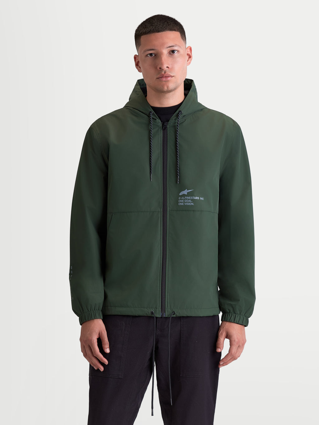 Alpinestars Giacca Frangivento Speeder Resolve, giacca con cappuccio da uomo verde pine, sportswear leggero per uso urbano, fodera in rete, cappuccio regolabile con coulisse e zip frontale, logo Alpinestars sul petto, vista frontale indossata.