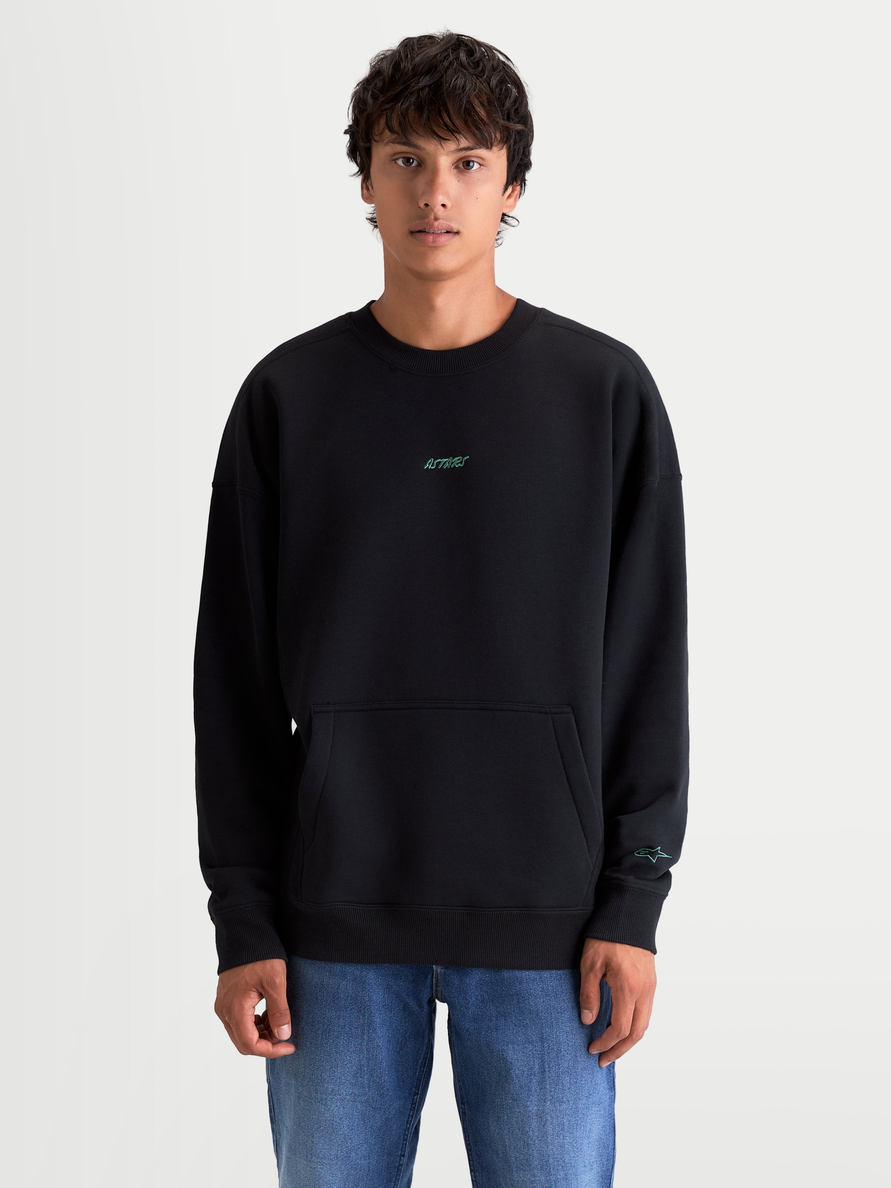 Alpinestars Guise Oversized Crew, felpa girocollo sportswear unisex, nera, vestibilità oversize con tasca a marsupio, loghi Astars ricamati verde acqua, in pile di cotone e poliestere riciclato, indossata da un modello.